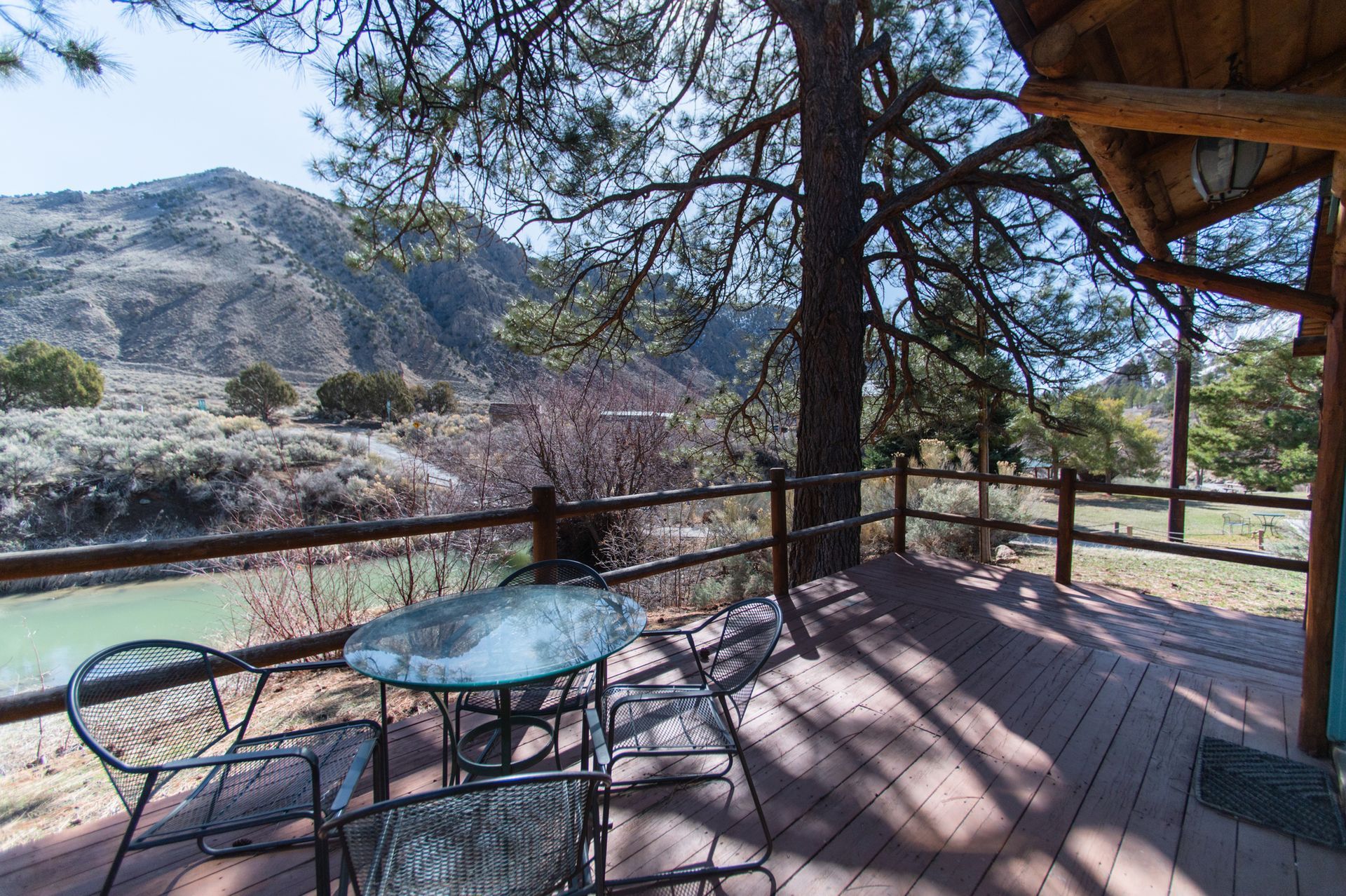 A deck with a table and chairs overlooking a river and mountains.