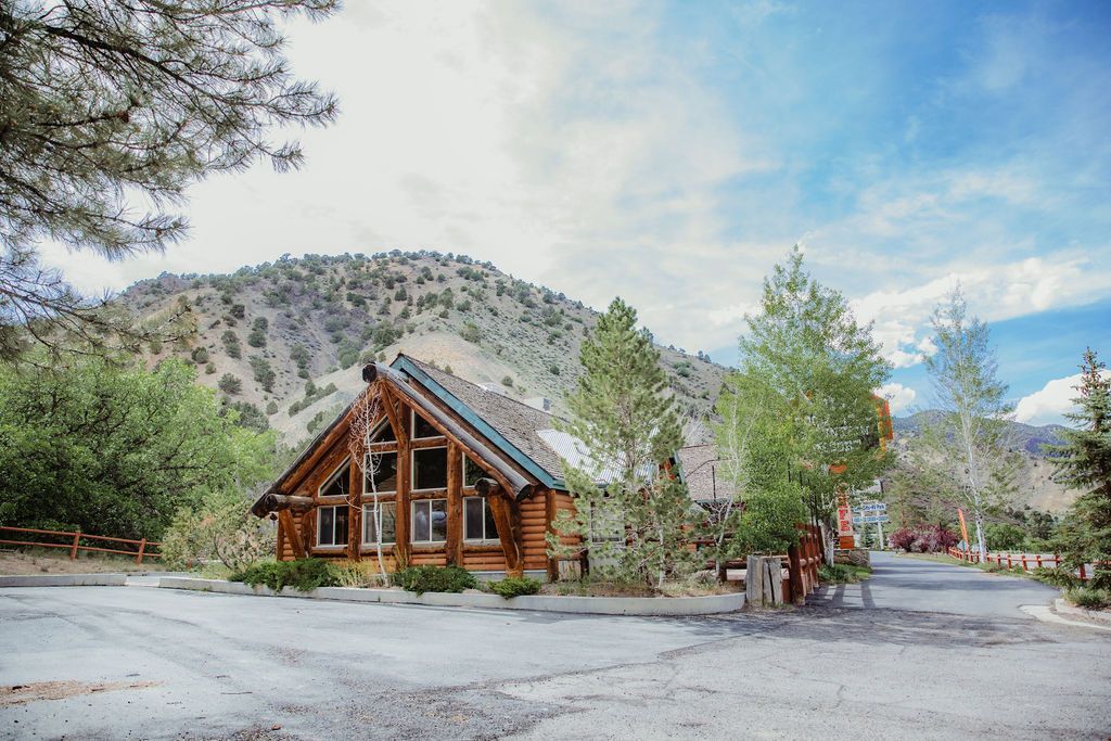 A log cabin in the middle of a forest with mountains in the background.