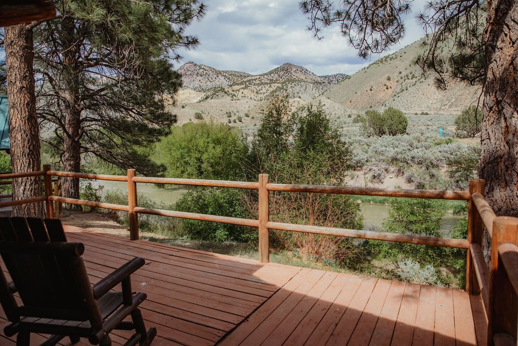 A wooden deck with rocking chairs and a fence overlooking a mountain range.