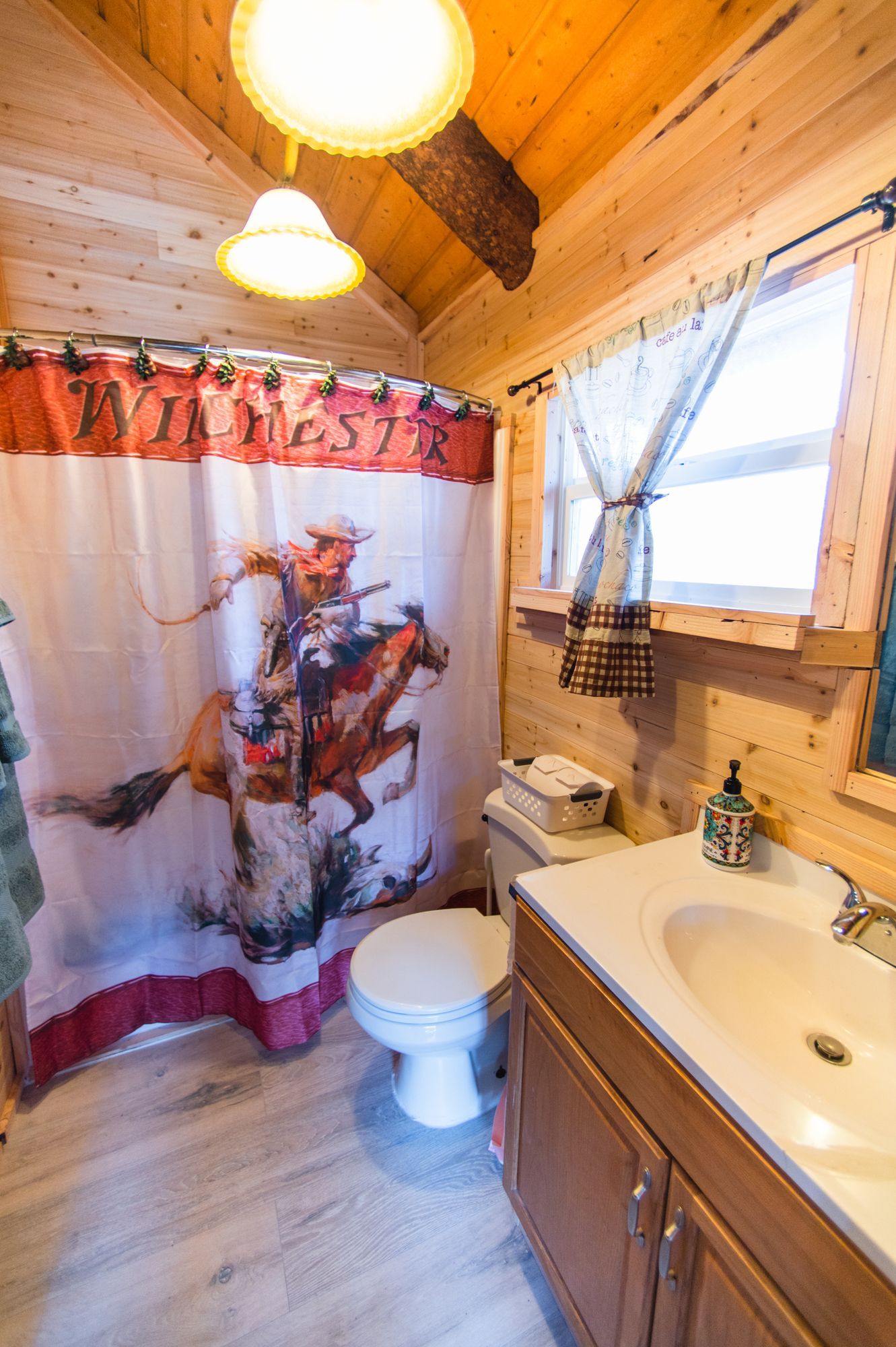 A bathroom with a toilet , sink and shower curtain with a cowboy on a horse.