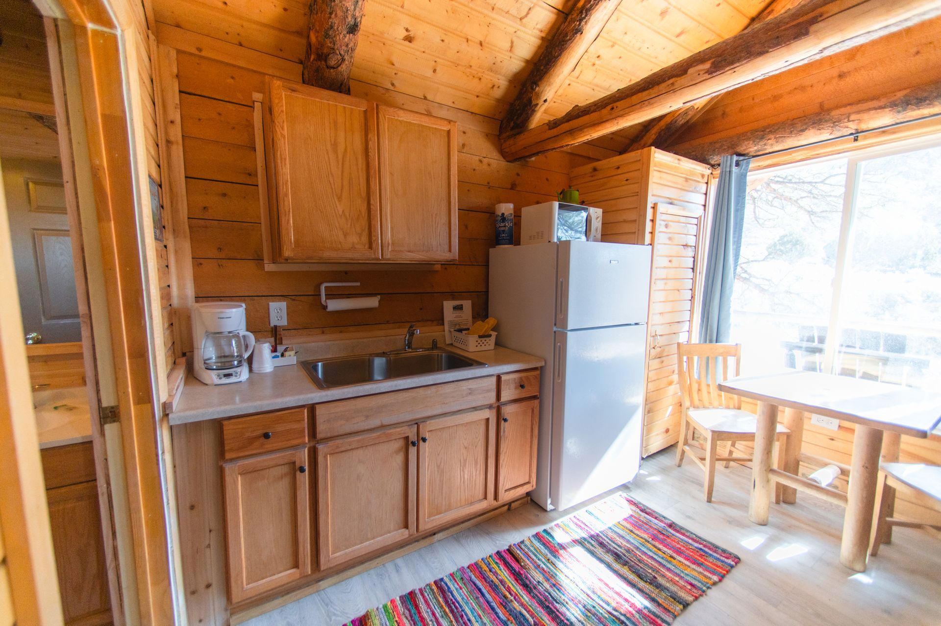 A kitchen in a log cabin with a refrigerator , sink , table and chairs.