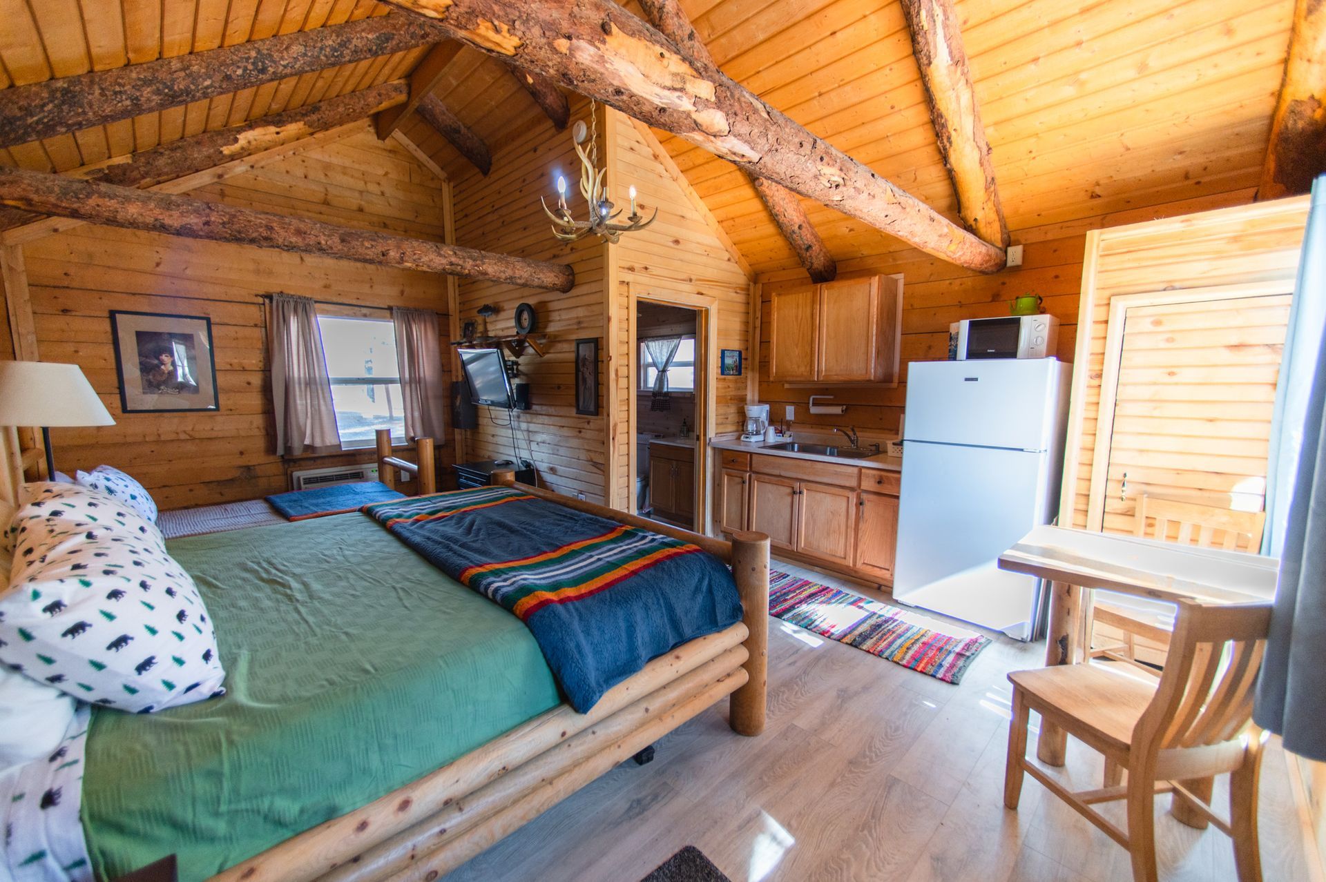 A bedroom in a log cabin with a bed , chair , table and refrigerator.