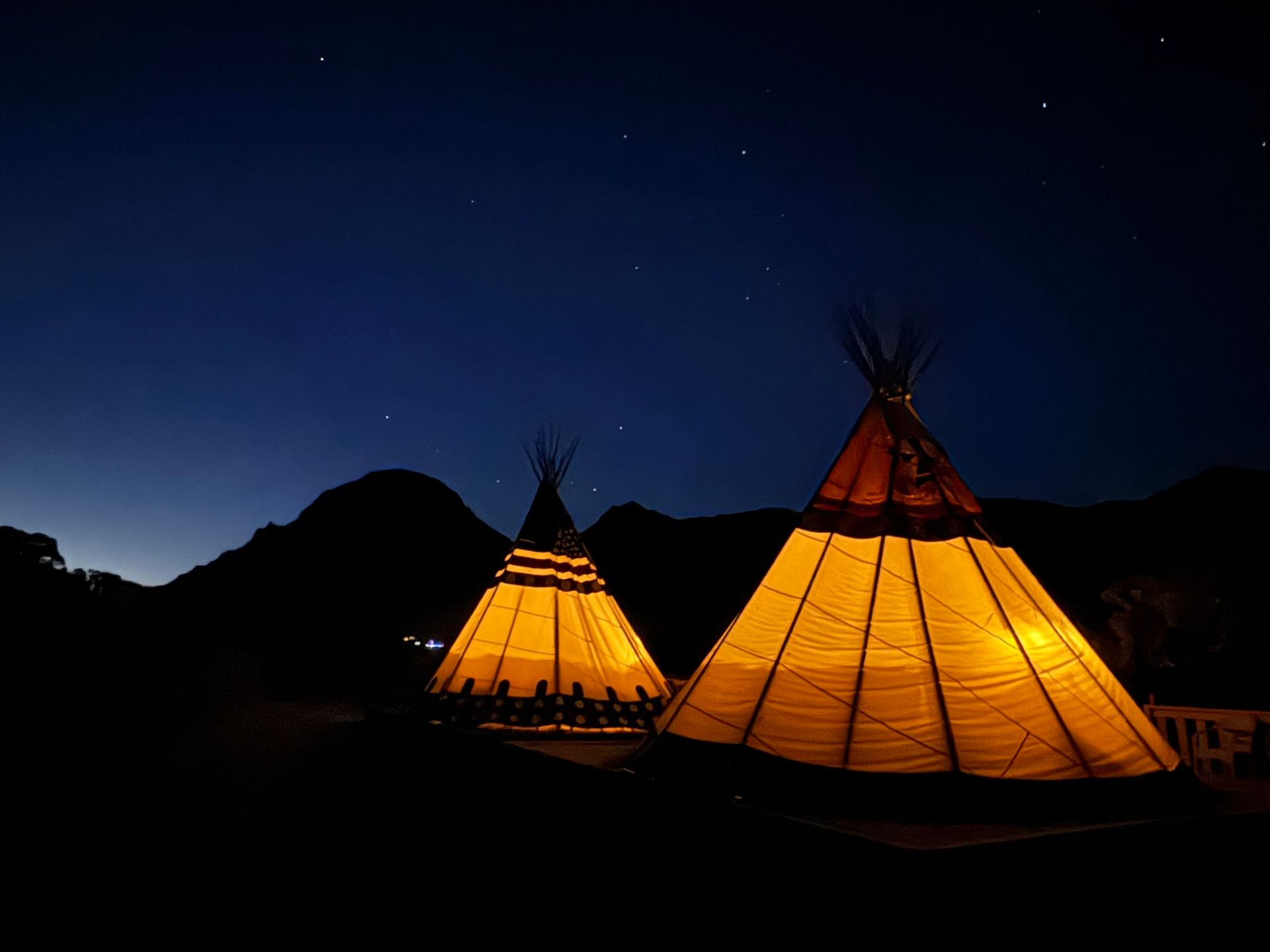 Two teepees are lit up at night under a starry sky