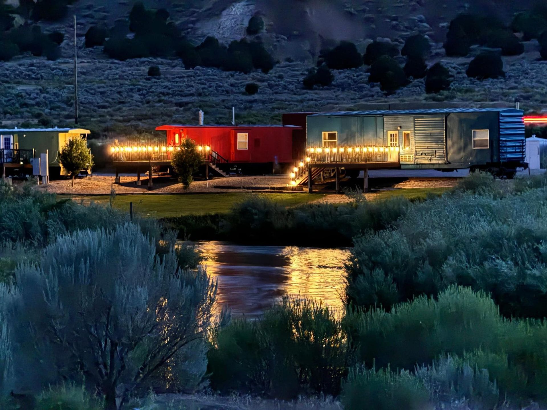 A train car is parked next to a river at night.