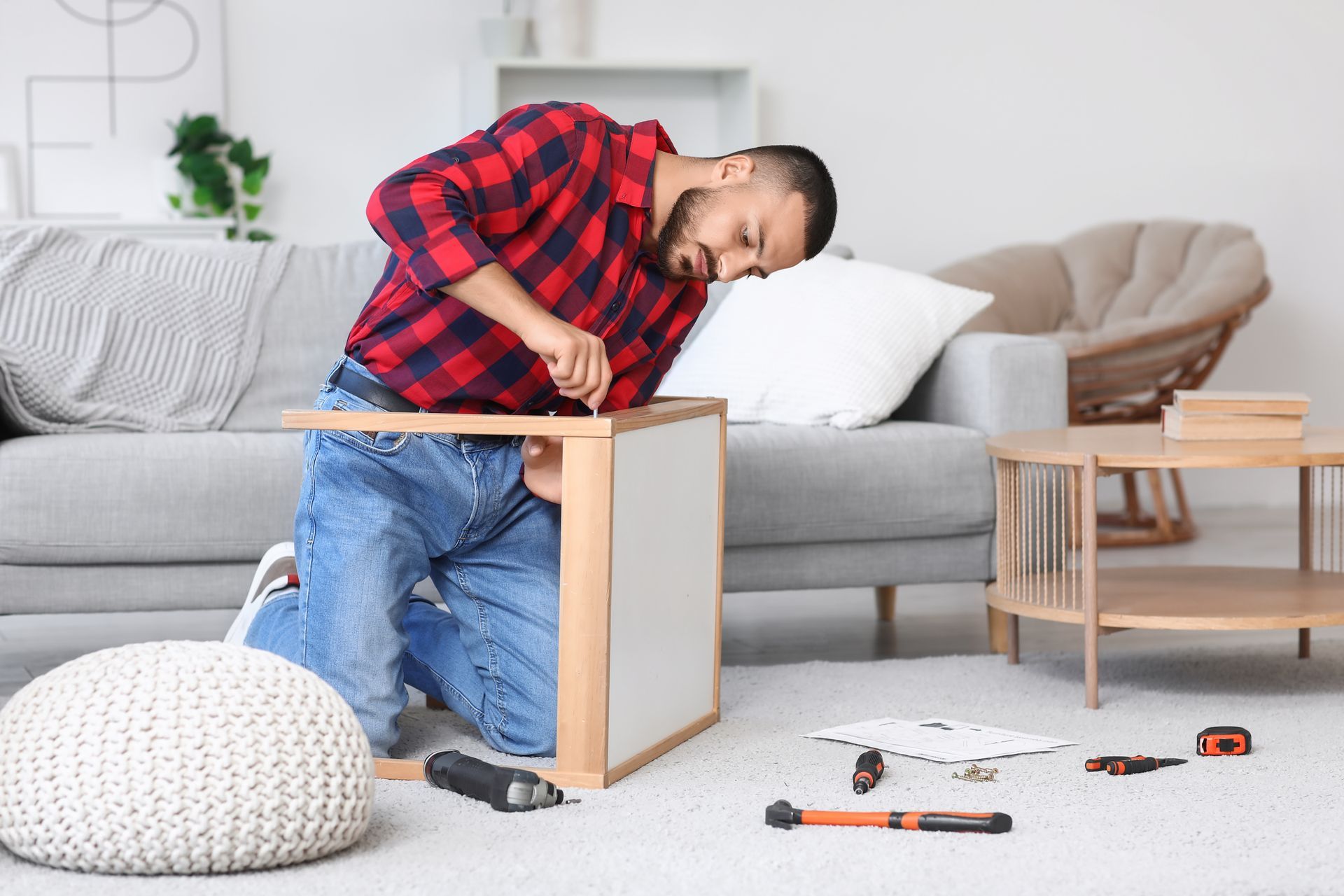 A man is kneeling on the floor in a living room while assembling a table.