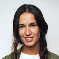 A woman with braided hair is smiling and wearing a green jacket.