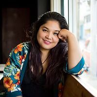 A woman is sitting in front of a window with her hand on her chin.