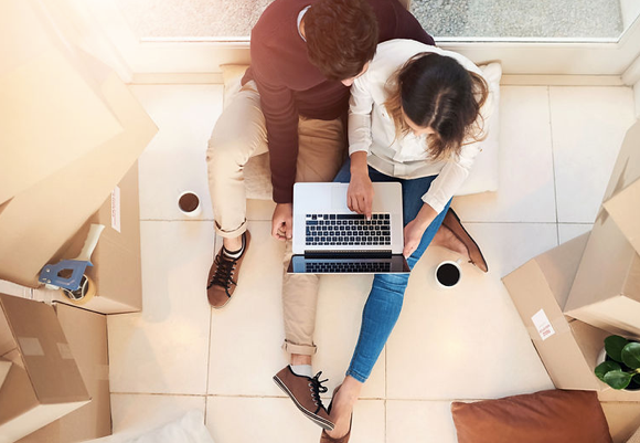 A man and a woman are sitting on the floor using a laptop computer.
