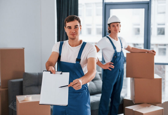 A man is holding a clipboard in front of a pile of cardboard boxes.