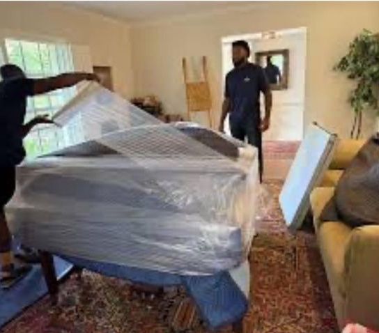 A man is wrapping a piano in plastic wrap in a living room.