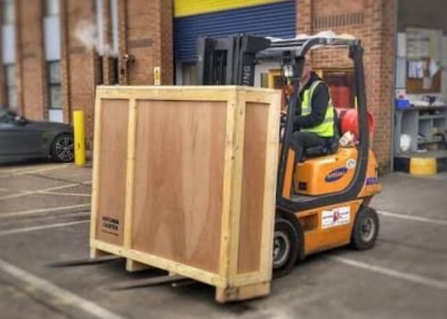 A forklift is carrying a large wooden box in a parking lot.