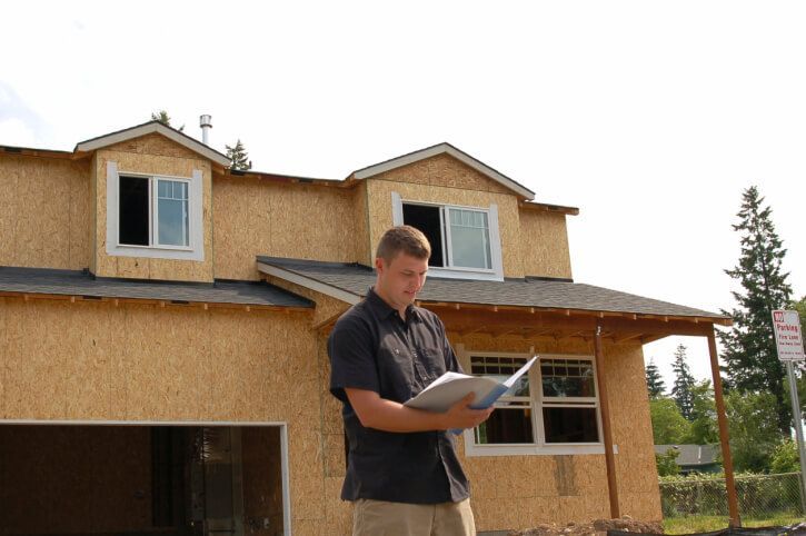 A man is reading a book in front of a house under construction