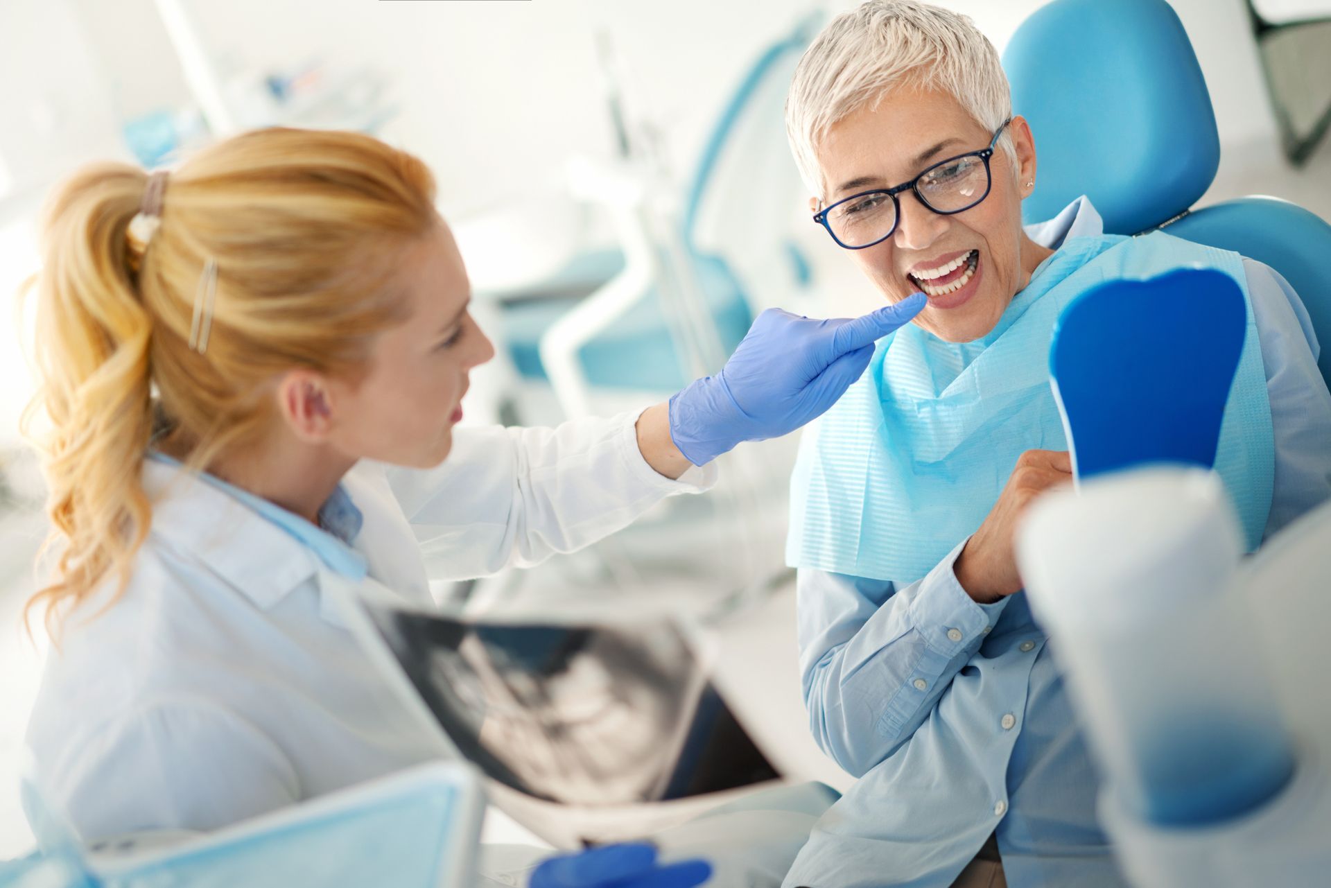 A dentist showing a smiling patient her teeth with a hand mirror in a dental office.