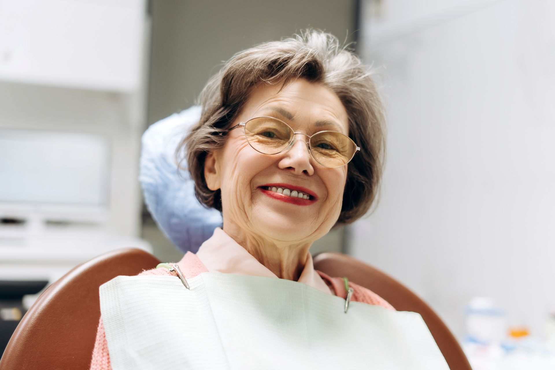 Woman with blonde hair smiling while seated in a dentist's chair. She is in a dental office.