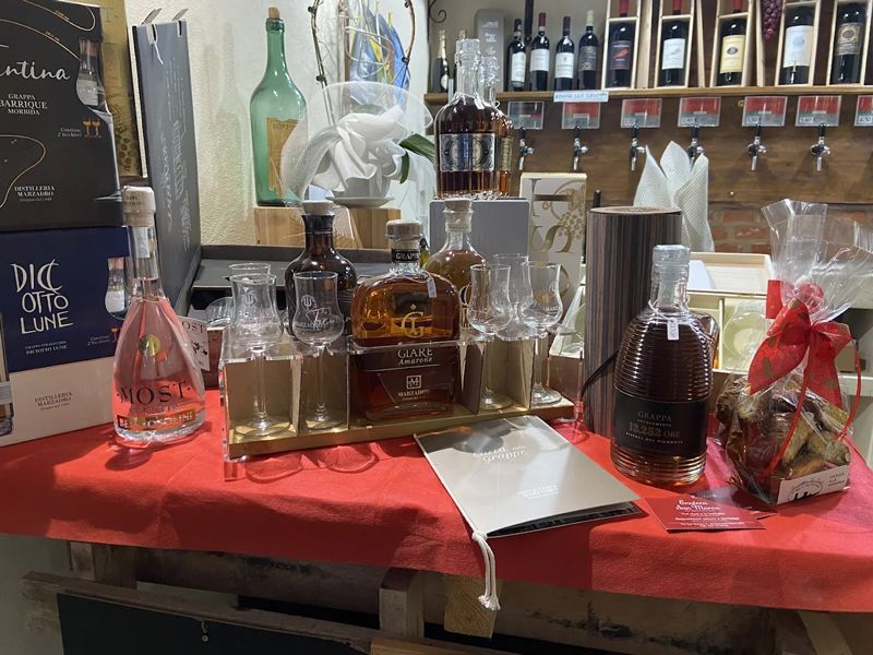 Esposizione di varie bottiglie di liquore e bicchieri su un tavolo rosso con un bar sullo sfondo.