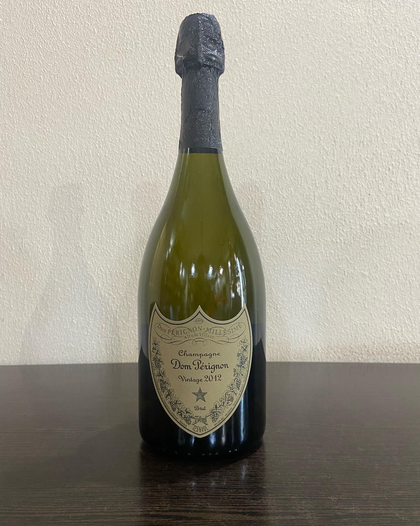 Bottiglia di champagne Dom Pérignon, vetro verde scuro, lamina nera, etichetta dorata.