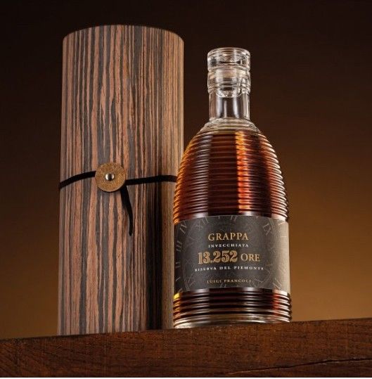 Bottiglia di Grappa in cassa di legno, liquido ambrato, etichetta visibile.