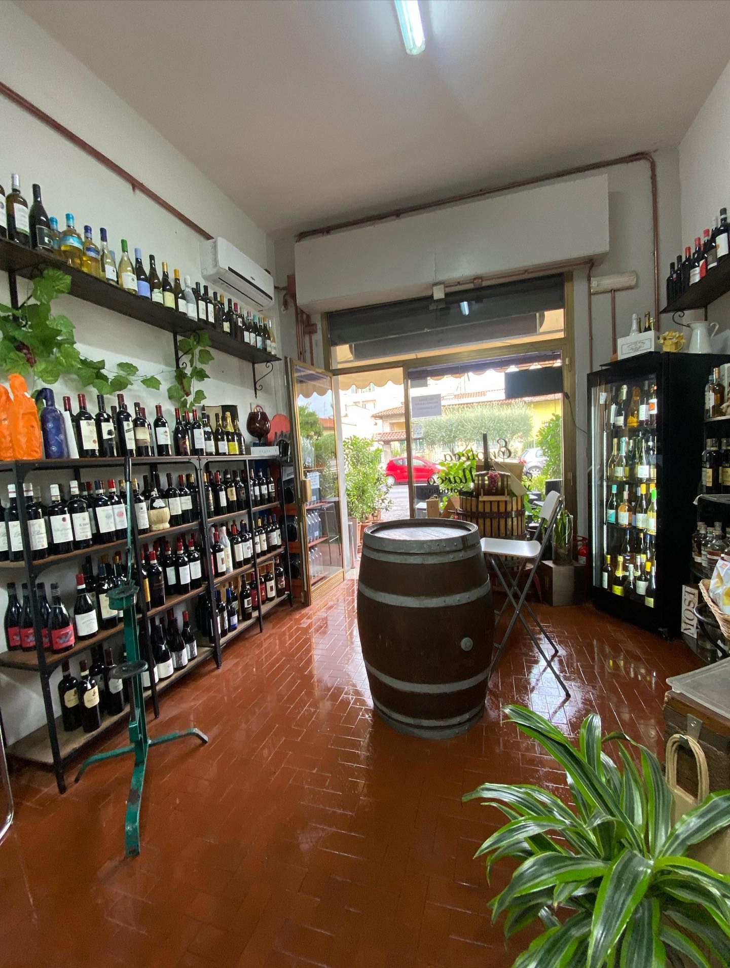 All'interno di un'enoteca, le bottiglie sono allineate sugli scaffali. Una grande botte è posizionata vicino alla porta aperta.