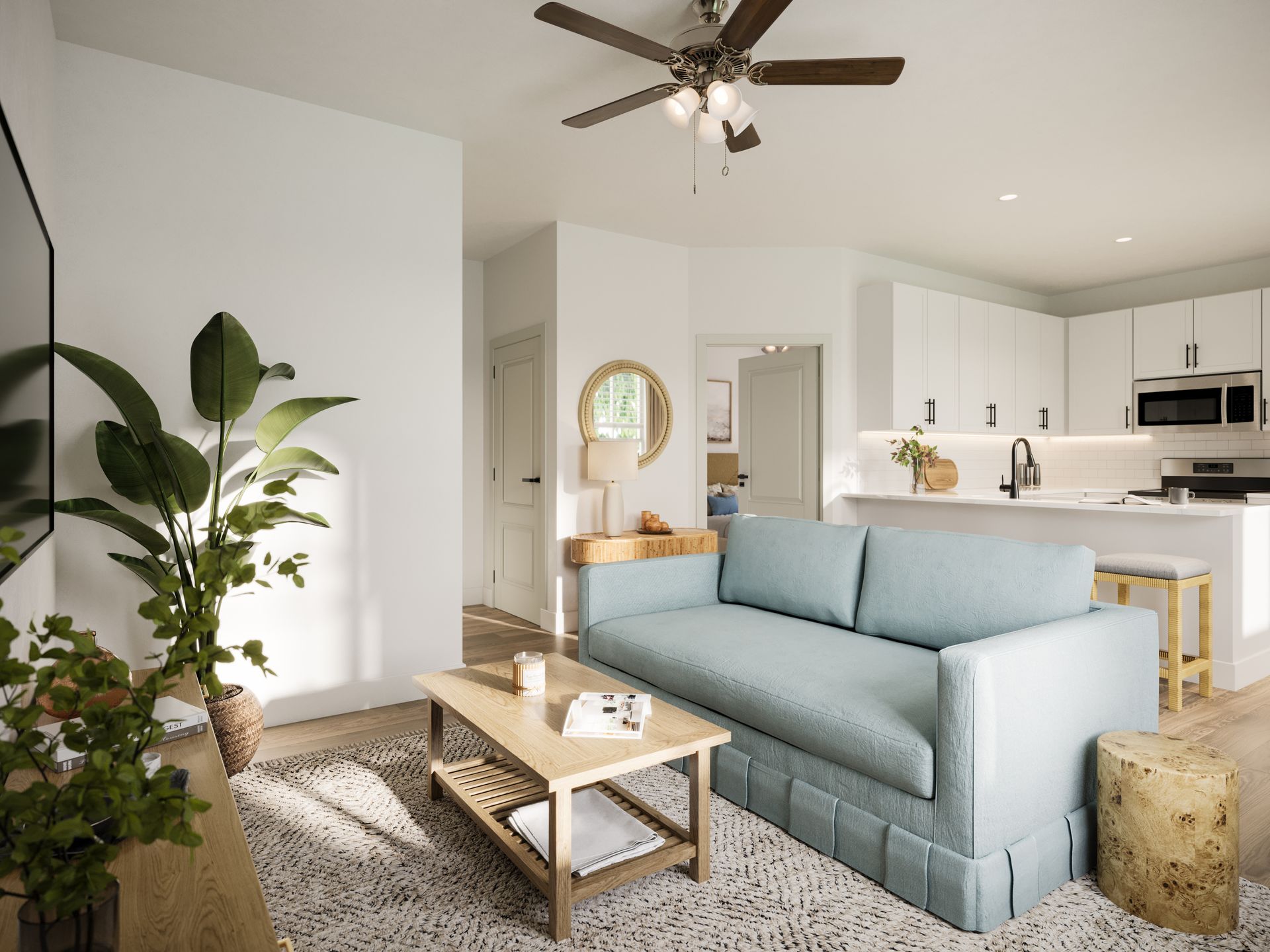 A sunlit living room featuring a light blue sofa, wood coffee table, potted plants, and a partial view of a white kitchen.