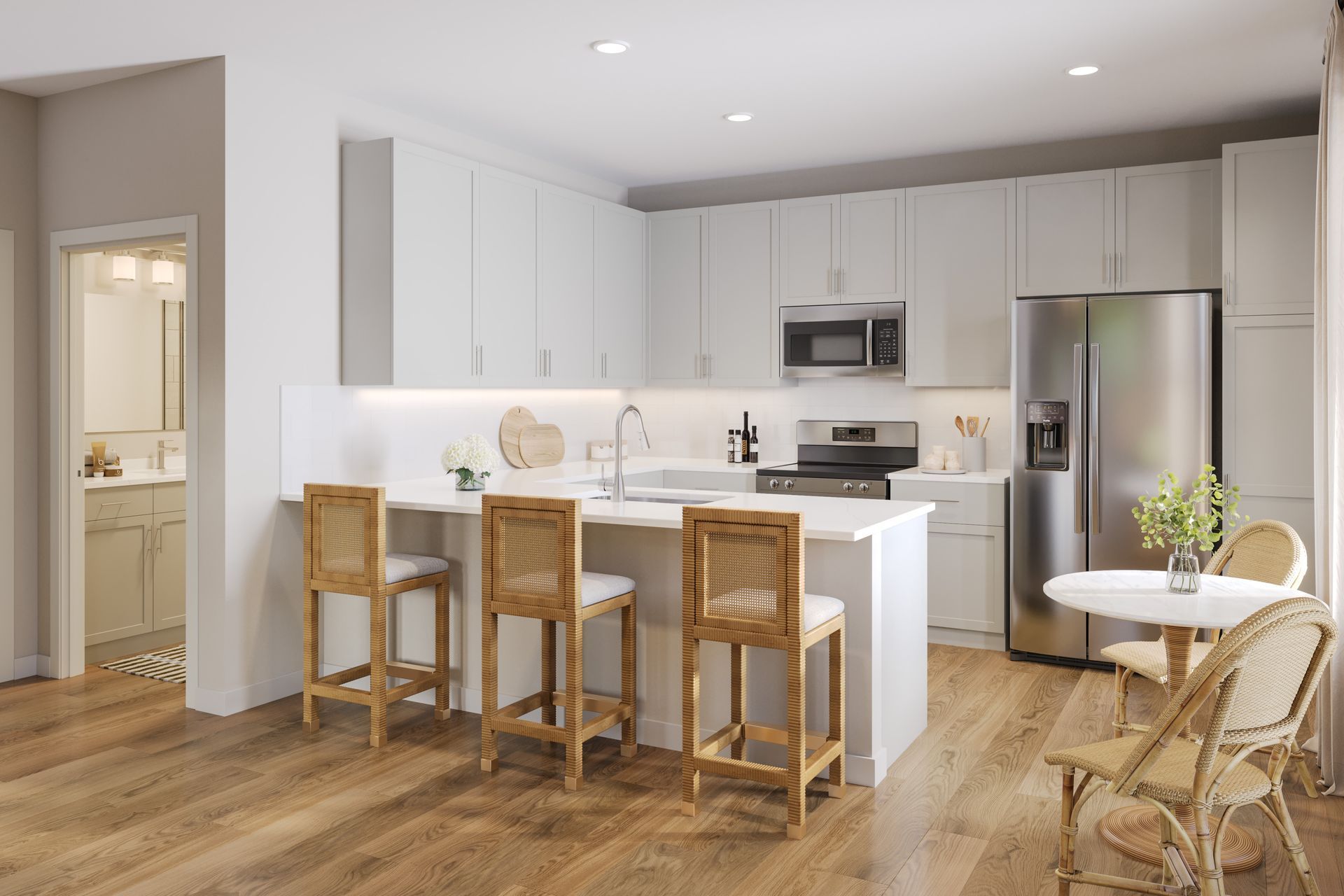 A modern kitchen with light gray cabinets, stainless steel appliances, a white island with three stools, and wood floors.