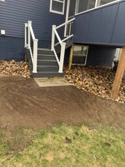 A dark blue house exterior with gray stairs leading to a deck, set against a yard with dirt and scattered leaves.
