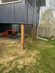 A low-angle view of a screened-in deck supported by wooden posts above a grassy backyard with a kayak and a downspout.