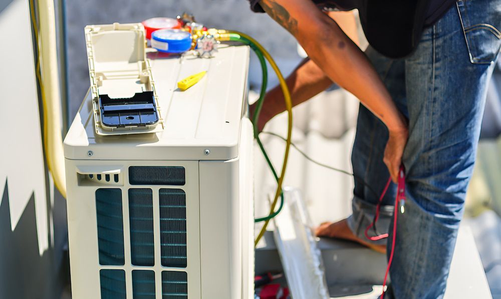 A Man Is Working On An Air Conditioner Outside — BT Airconditioning In Portsmith, QLD