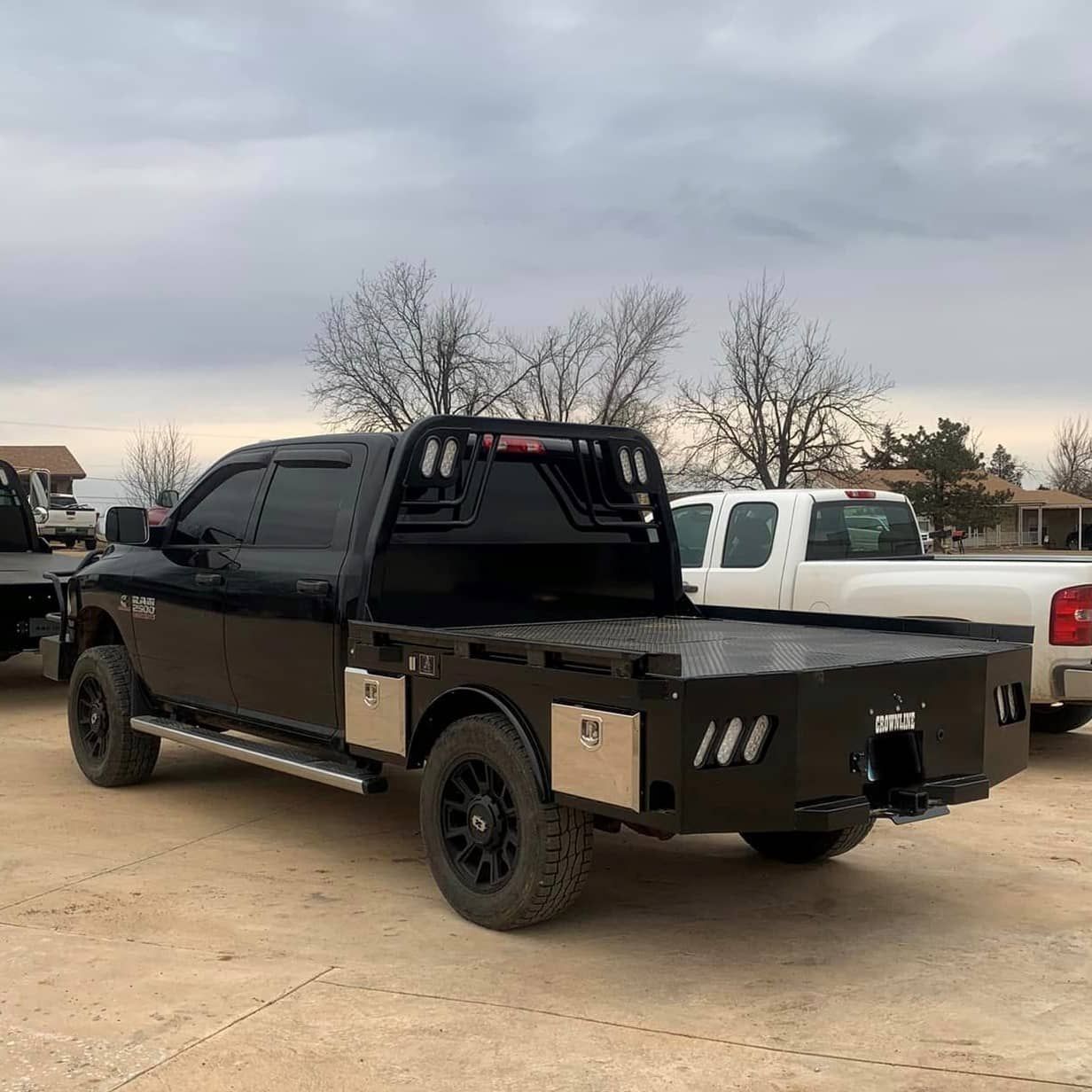 A black truck with skirted flatbed parked in a dirt lot next to a white truck.