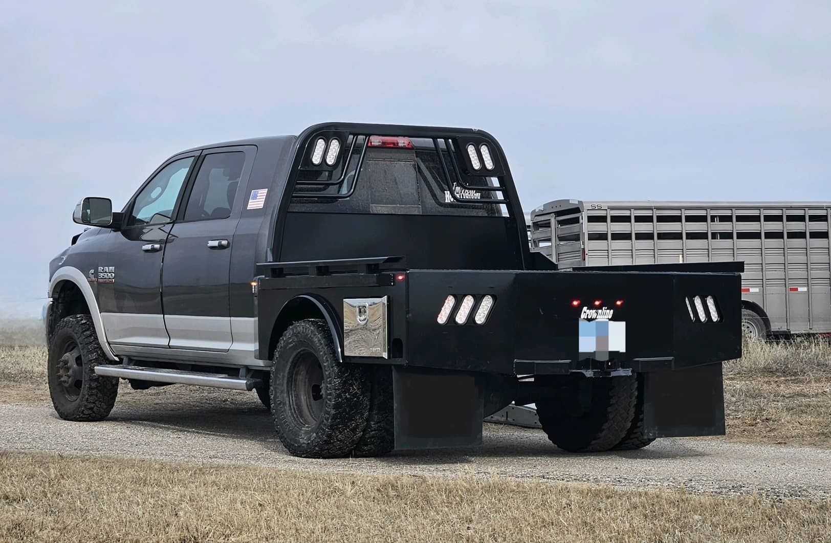 A black ram mega cab truck with a skirted flat bed with toolboxes is parked in a field.