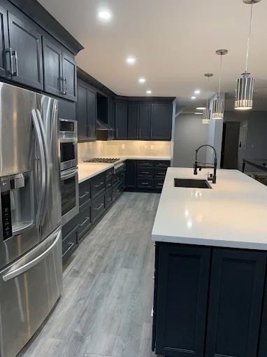 Modern kitchen with dark cabinets, stainless steel appliances, white island, and recessed lighting.