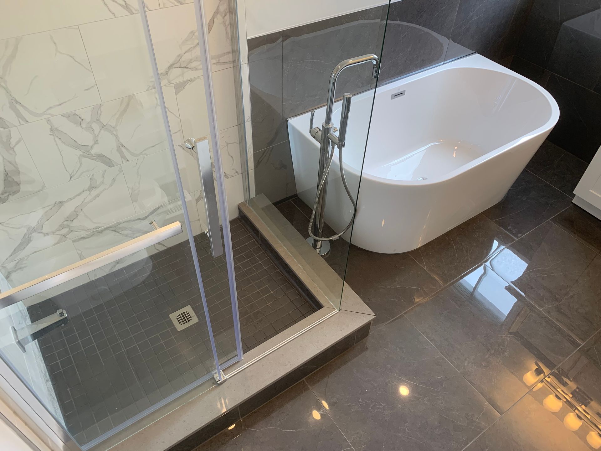 Modern bathroom with glass shower, white freestanding tub, and dark tiled floor
