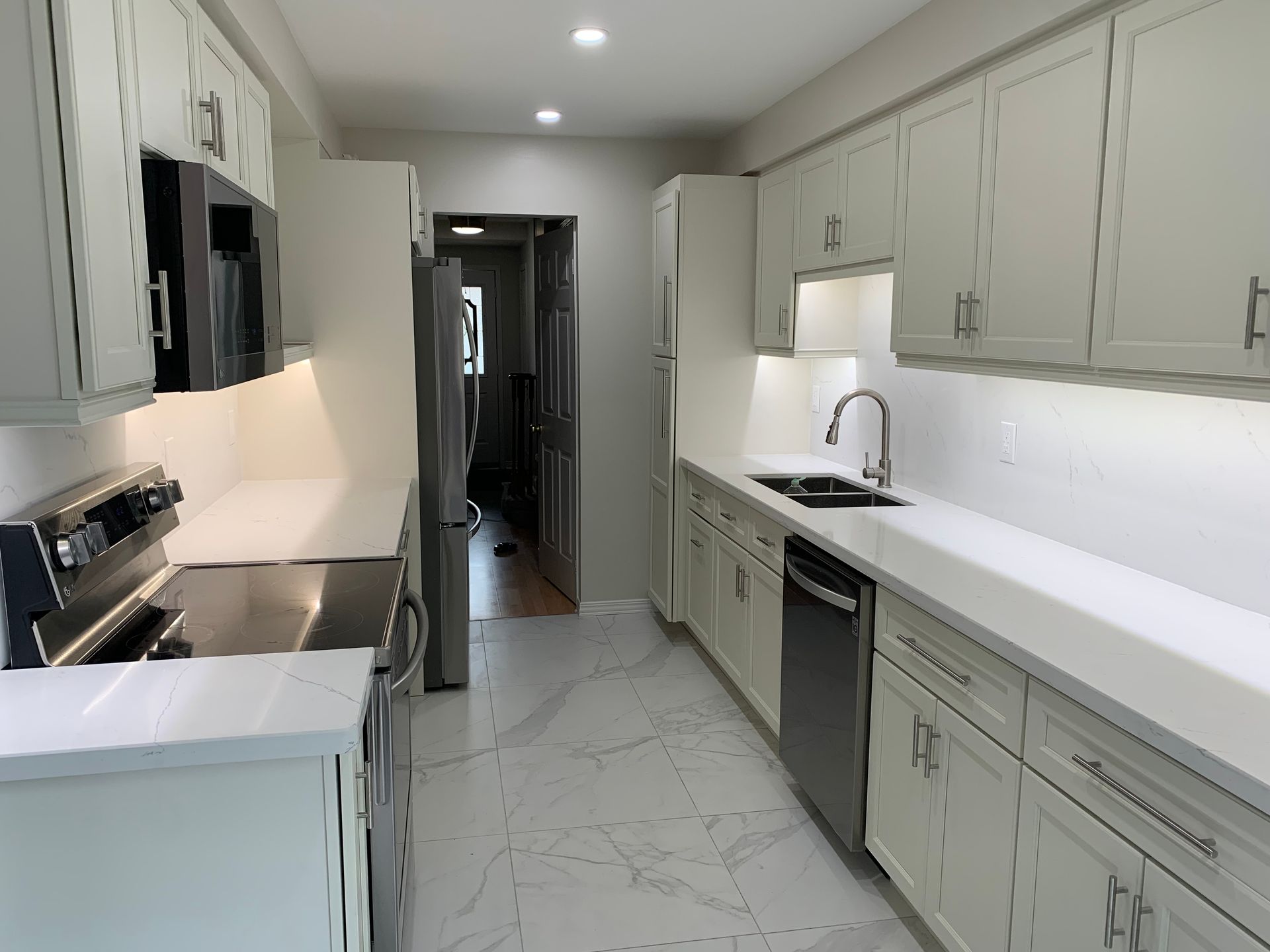 Modern white galley kitchen with stainless appliances, gray cabinets, and marble-patterned floor.