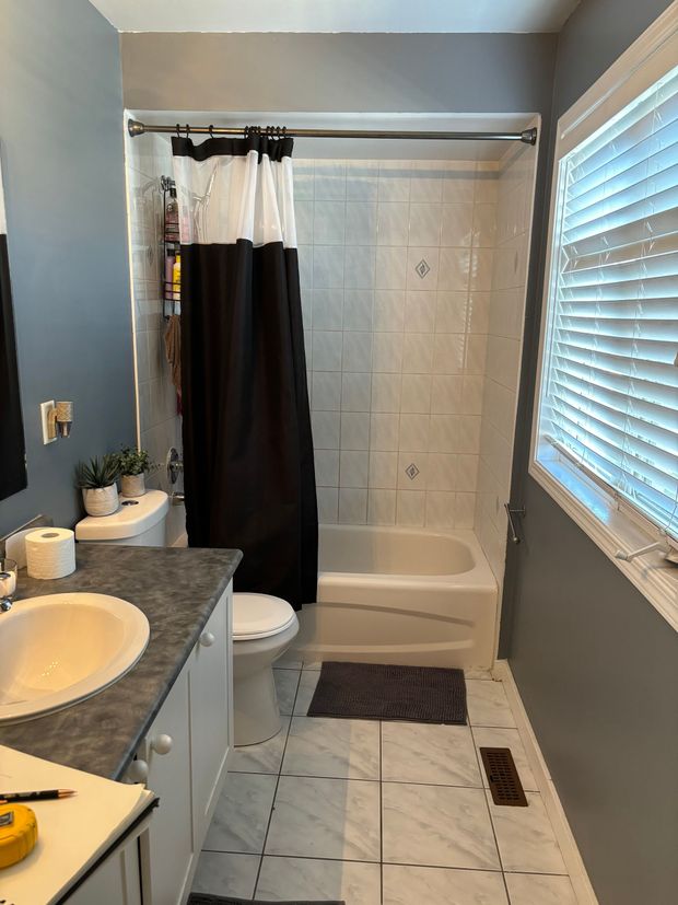 Bathroom with white tub and shower curtain, gray walls, vanity sink, window blinds, and tiled floor