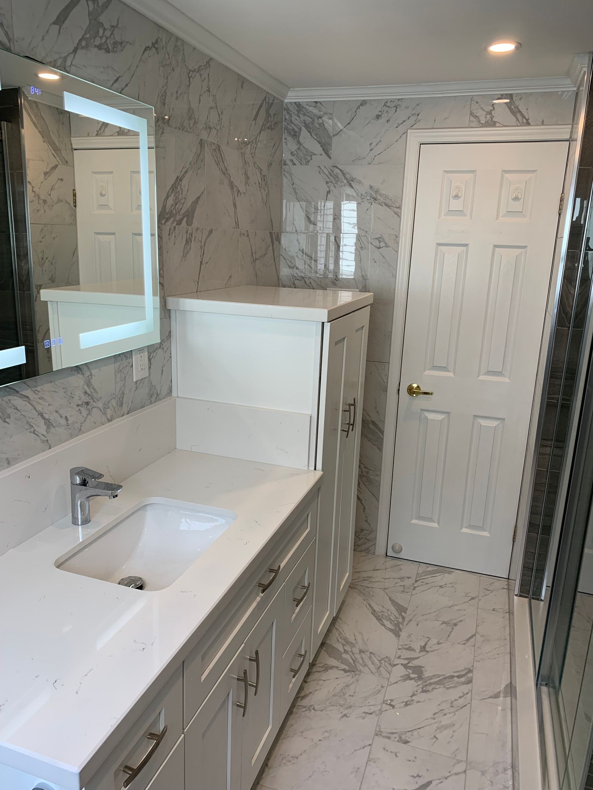 Modern bathroom with marble walls, white vanity, lit mirror, and a closed door