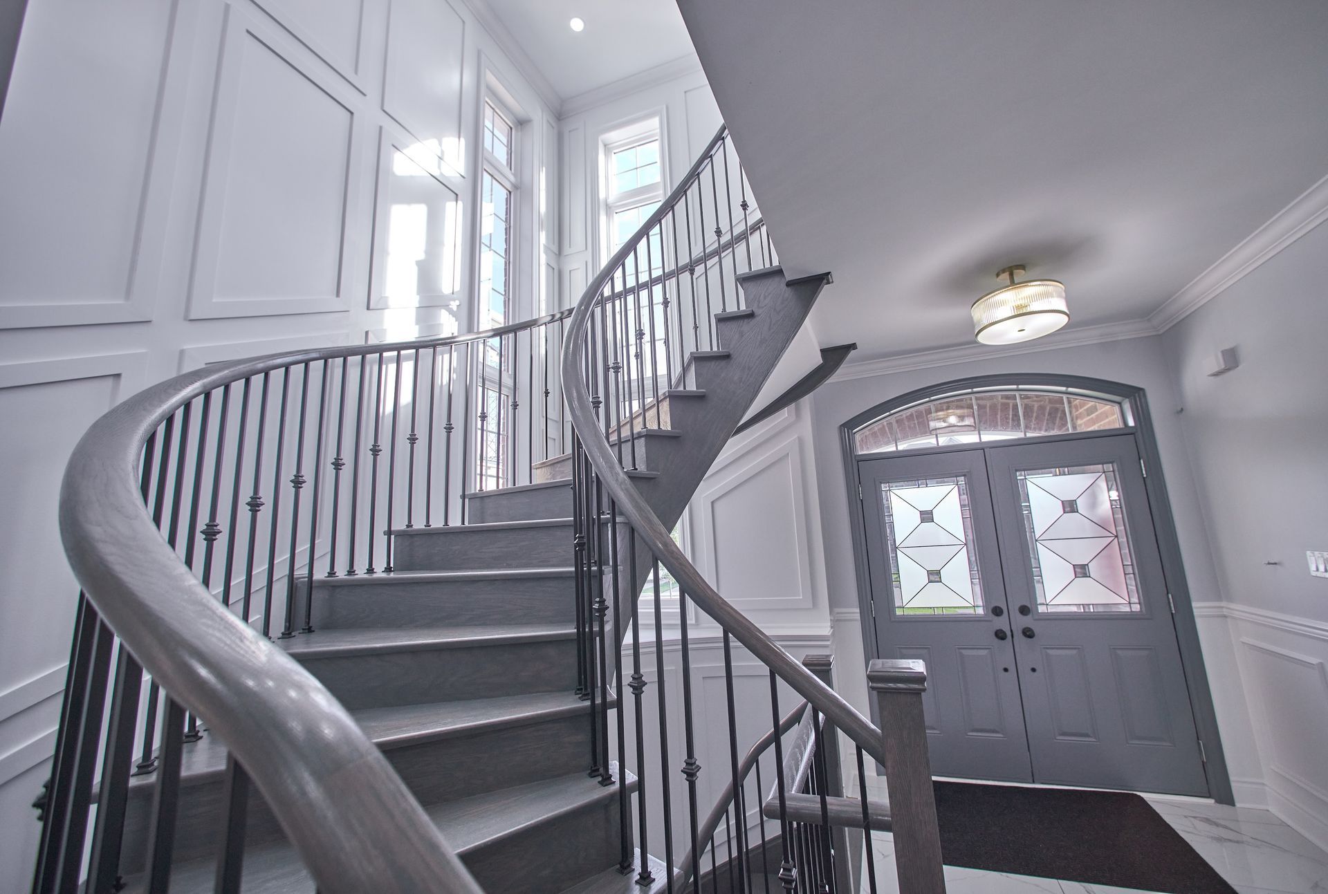 Curved staircase in a white entryway with a gray front door and decorative glass