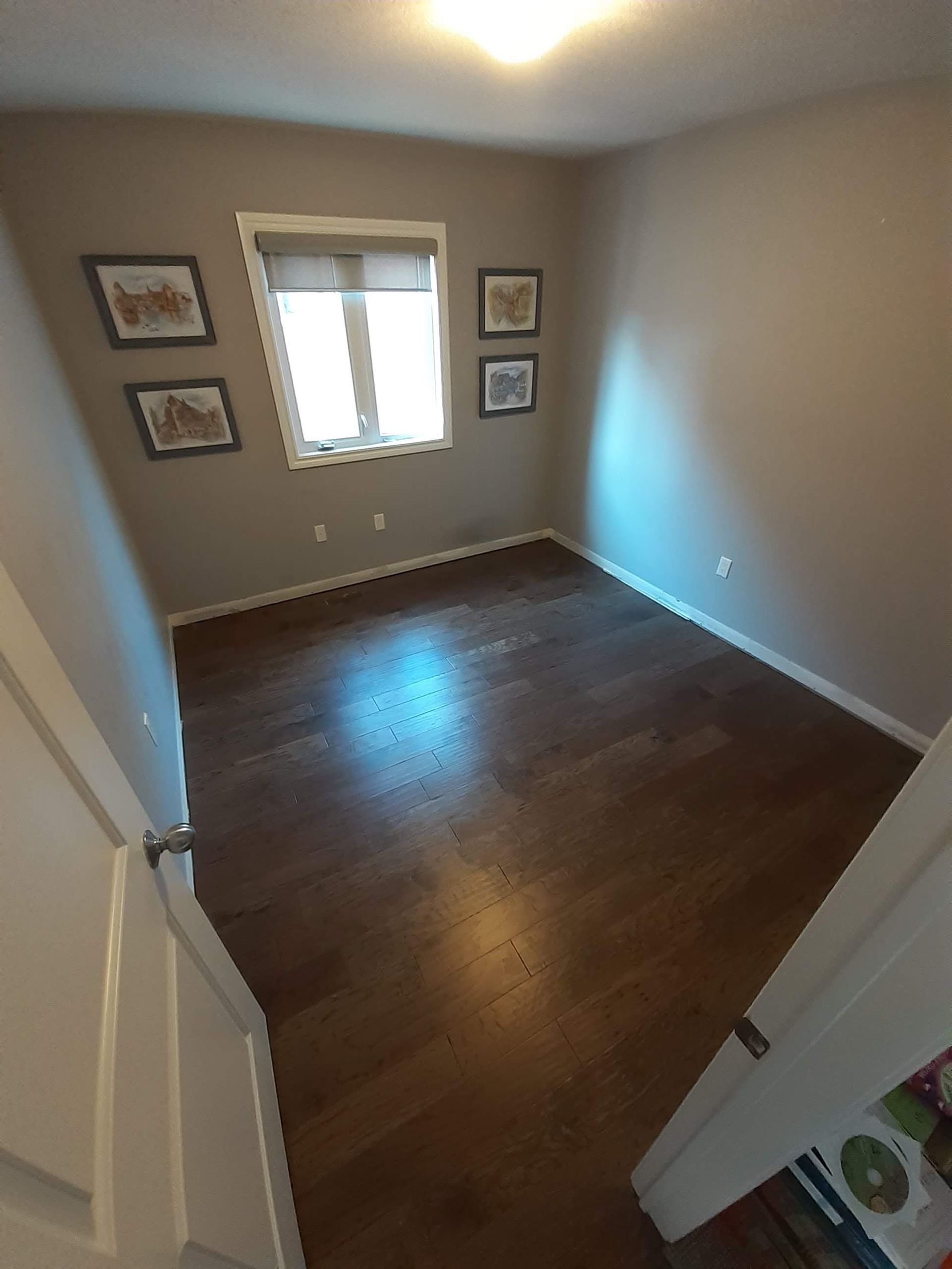 Empty beige bedroom with dark wood floors, window, and framed wall art