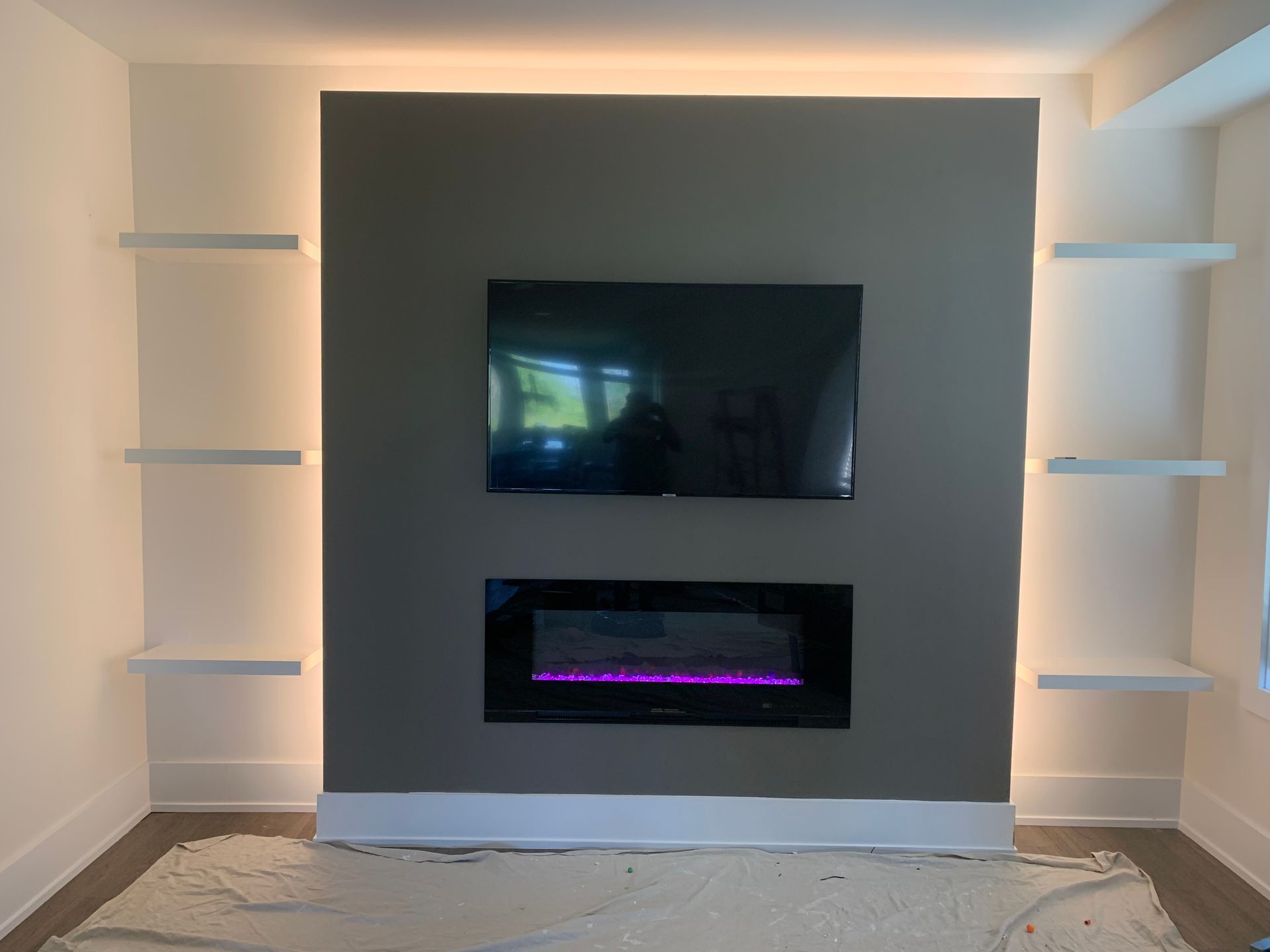 Modern living room with wall-mounted TV above an electric fireplace and floating shelves on both sides