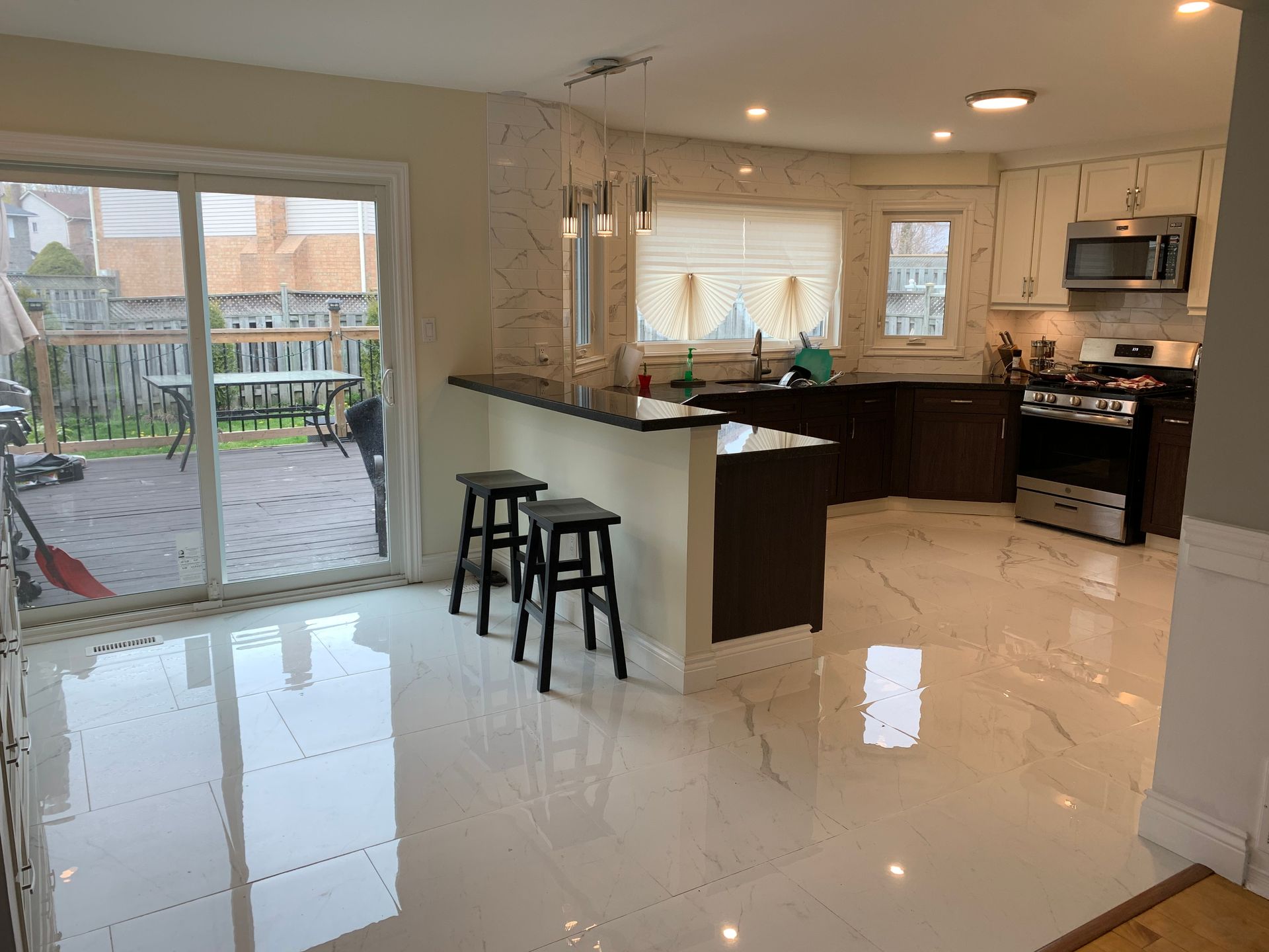 Bright kitchen with white tile floor, dark cabinets, island stools, and sliding glass doors to a backyard.