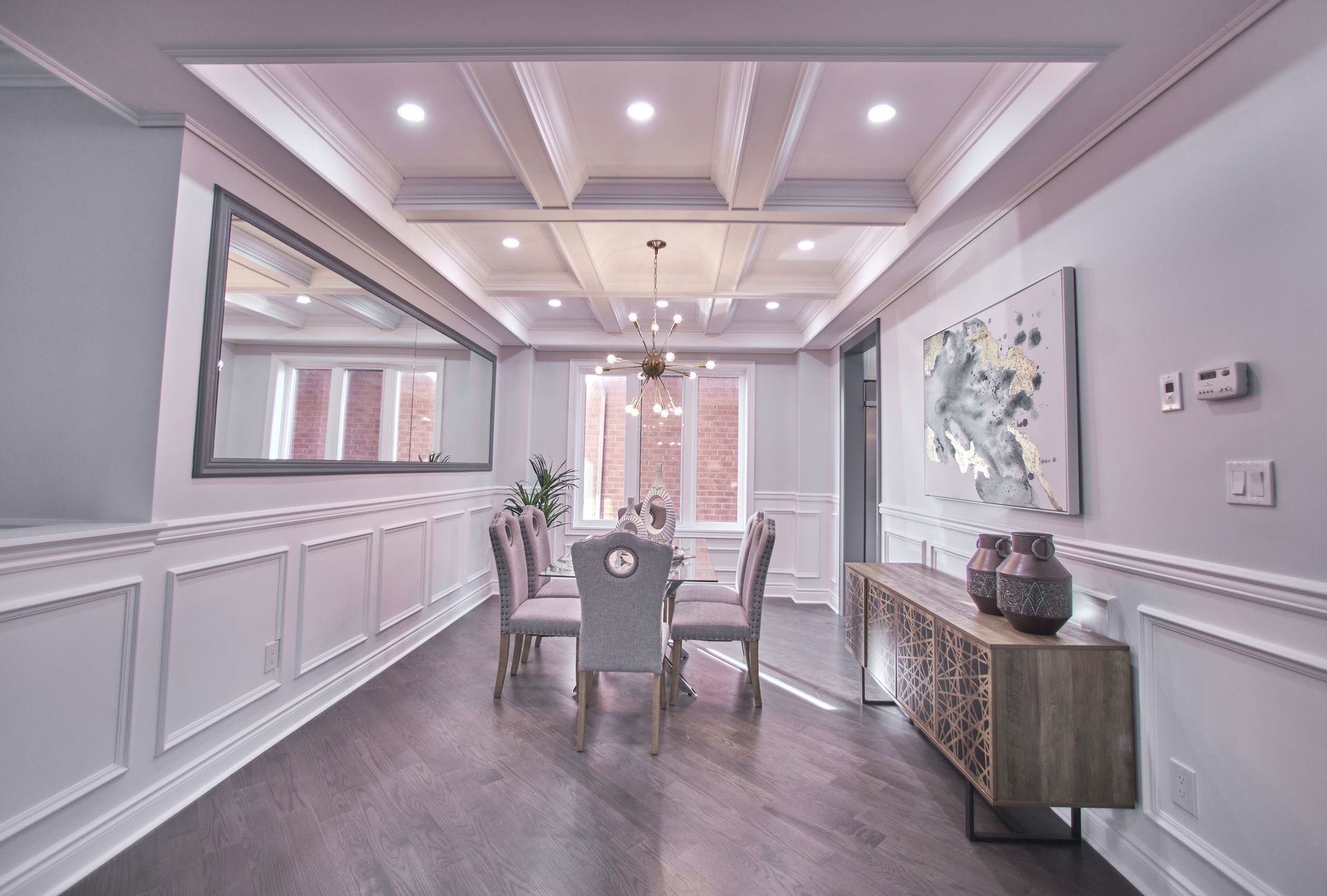 Elegant dining room with white paneled walls, chandelier lighting, and a wooden table under a large mirror.