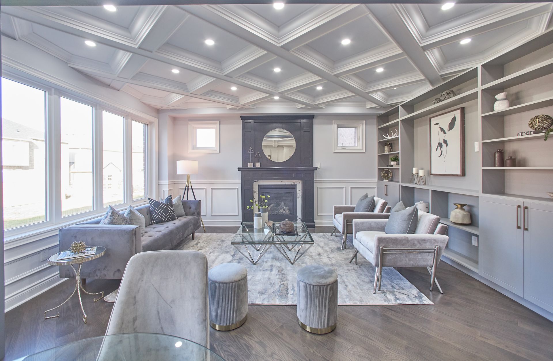 Bright modern living room with gray sofas, patterned chairs, a fireplace, and large windows