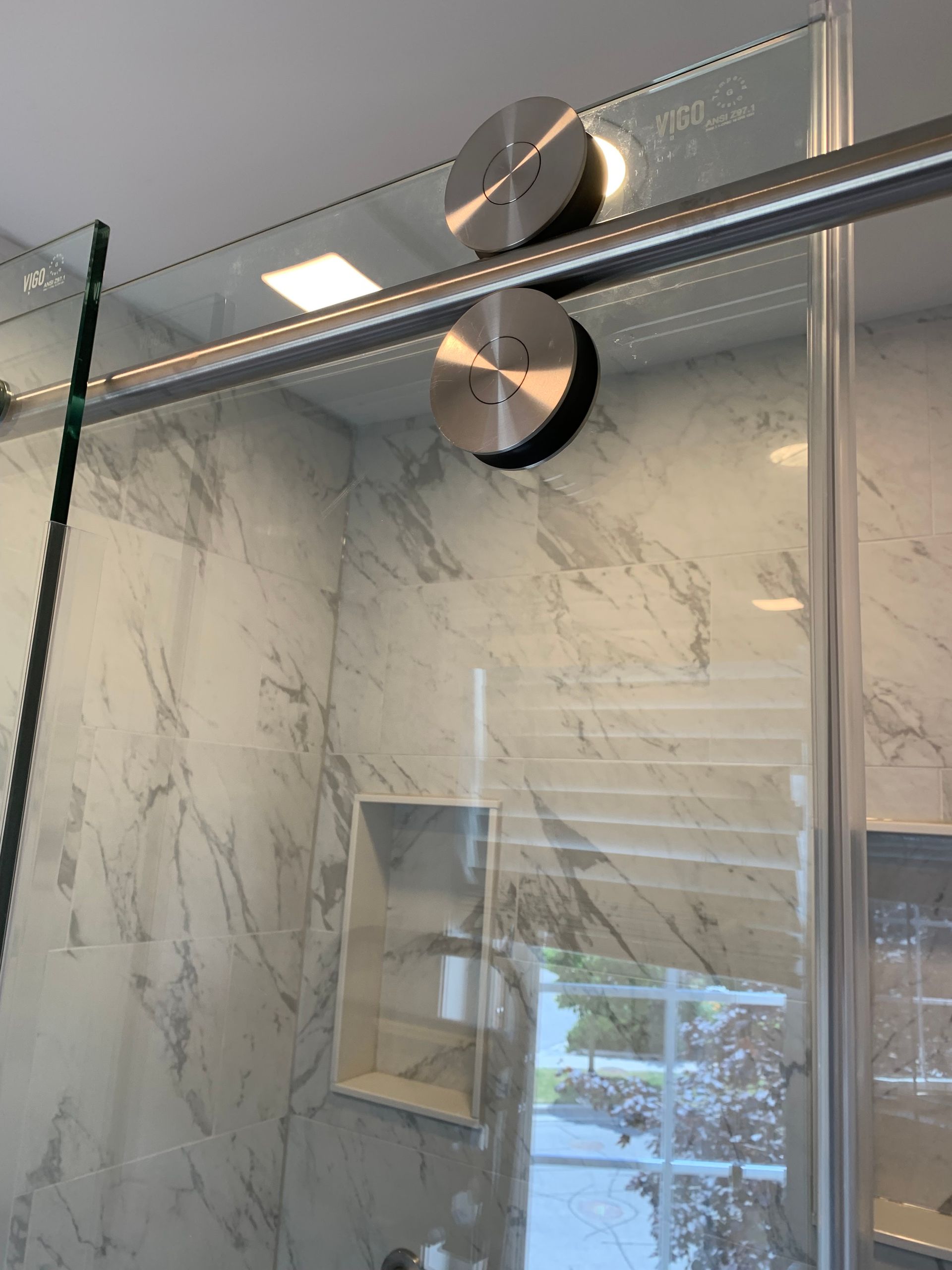 Glass shower door with chrome hardware and marble-patterned tile wall in a bathroom