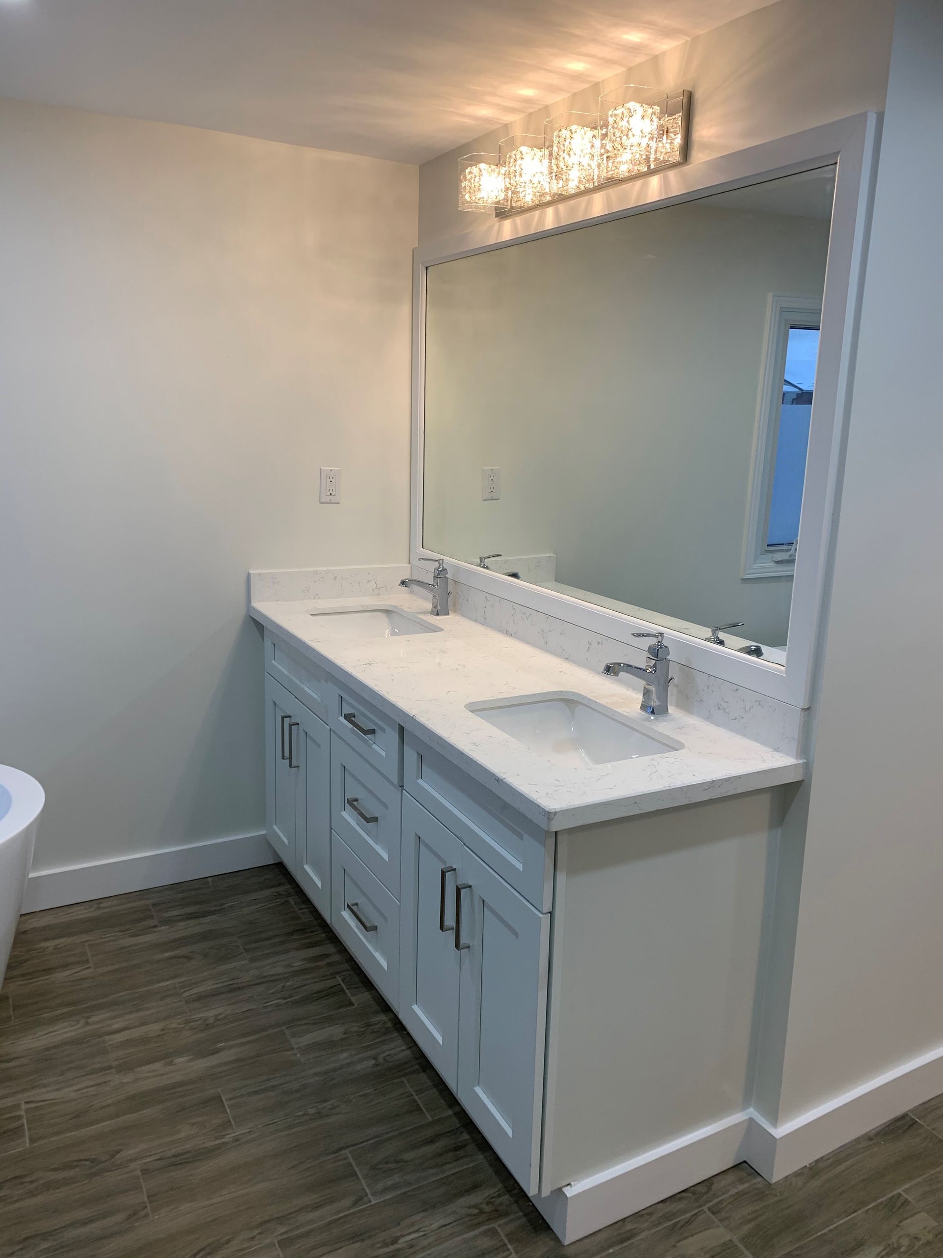 Modern bathroom vanity with white countertop, large mirror, and lit vanity lights.