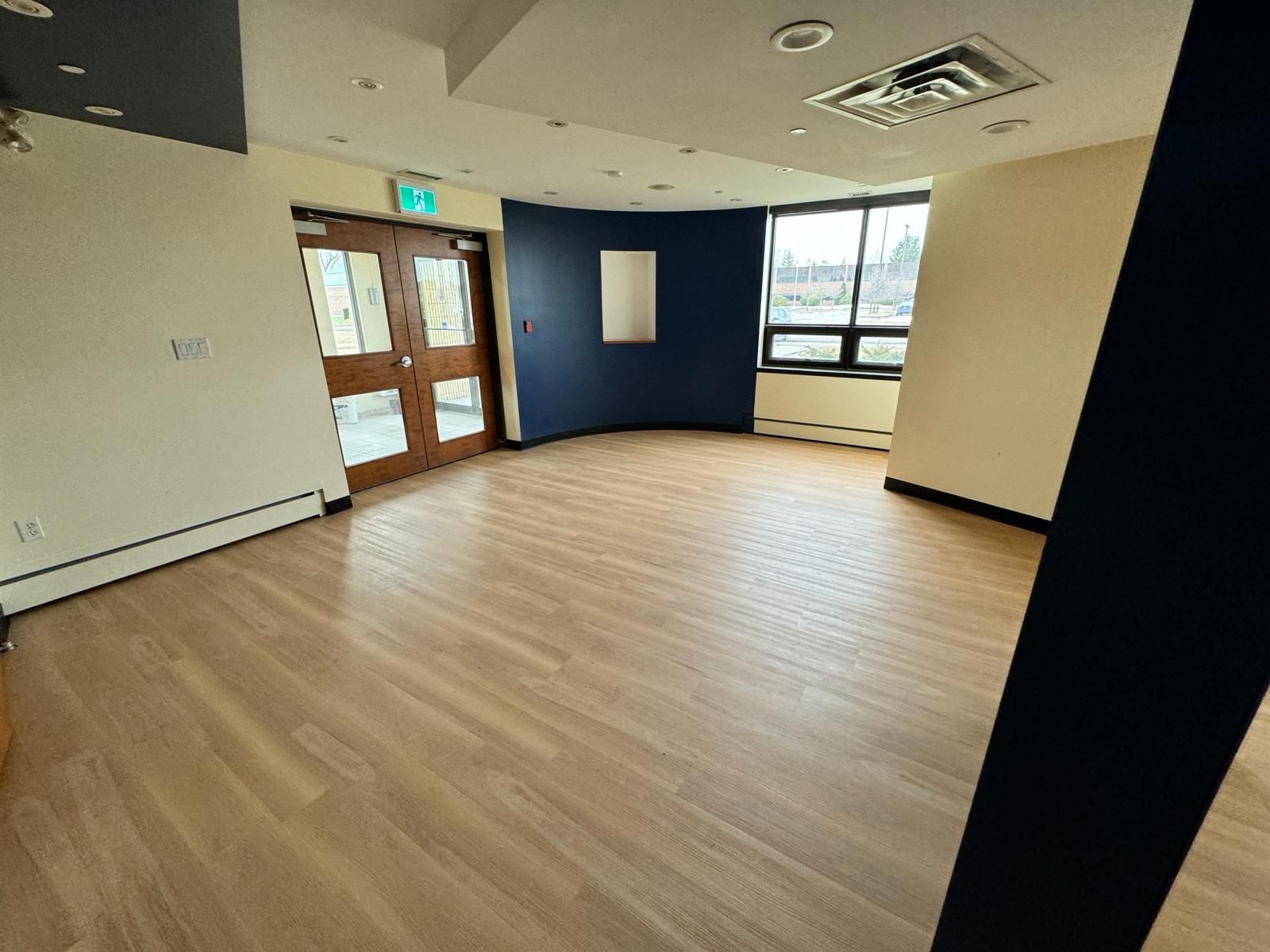 Empty office room with wood floor, blue accent wall, and windows near a glass door