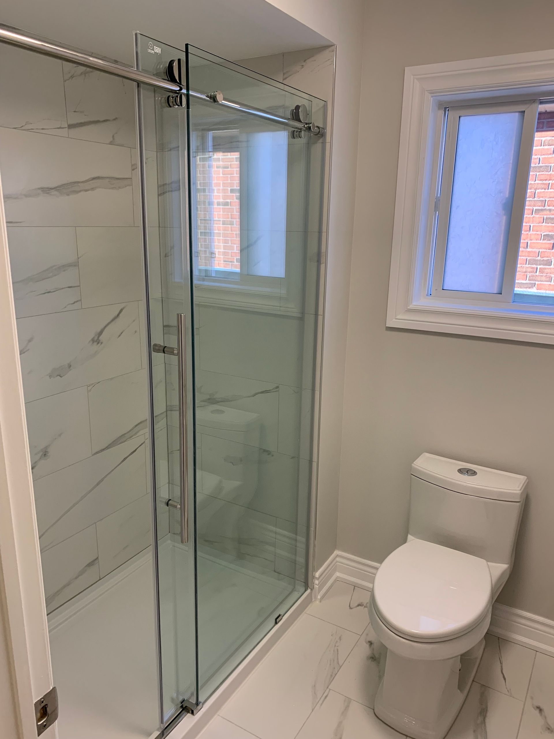 Small bathroom with glass shower enclosure, white toilet, and two windows.