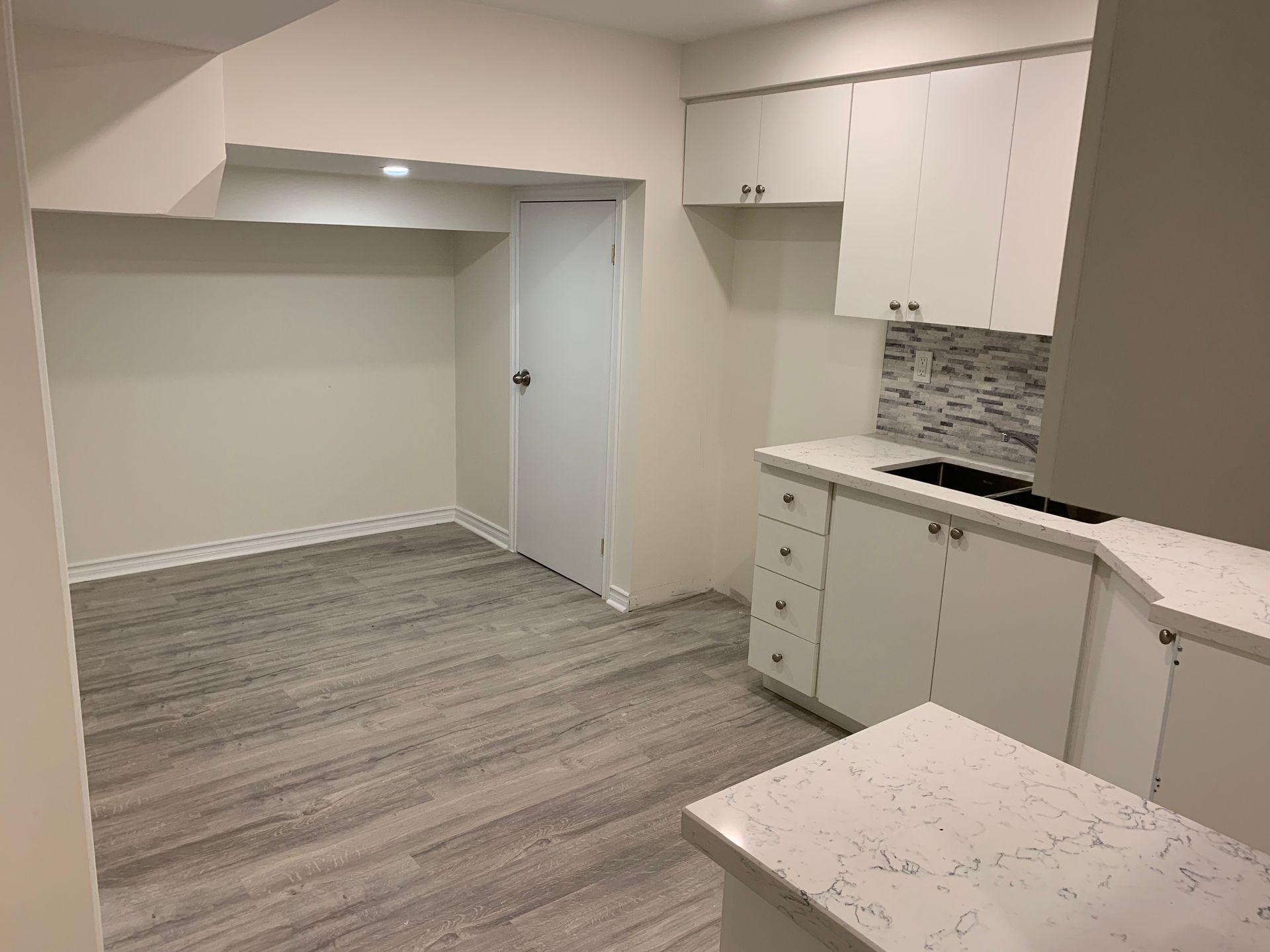 Empty modern kitchen and dining nook with white cabinets and gray wood flooring