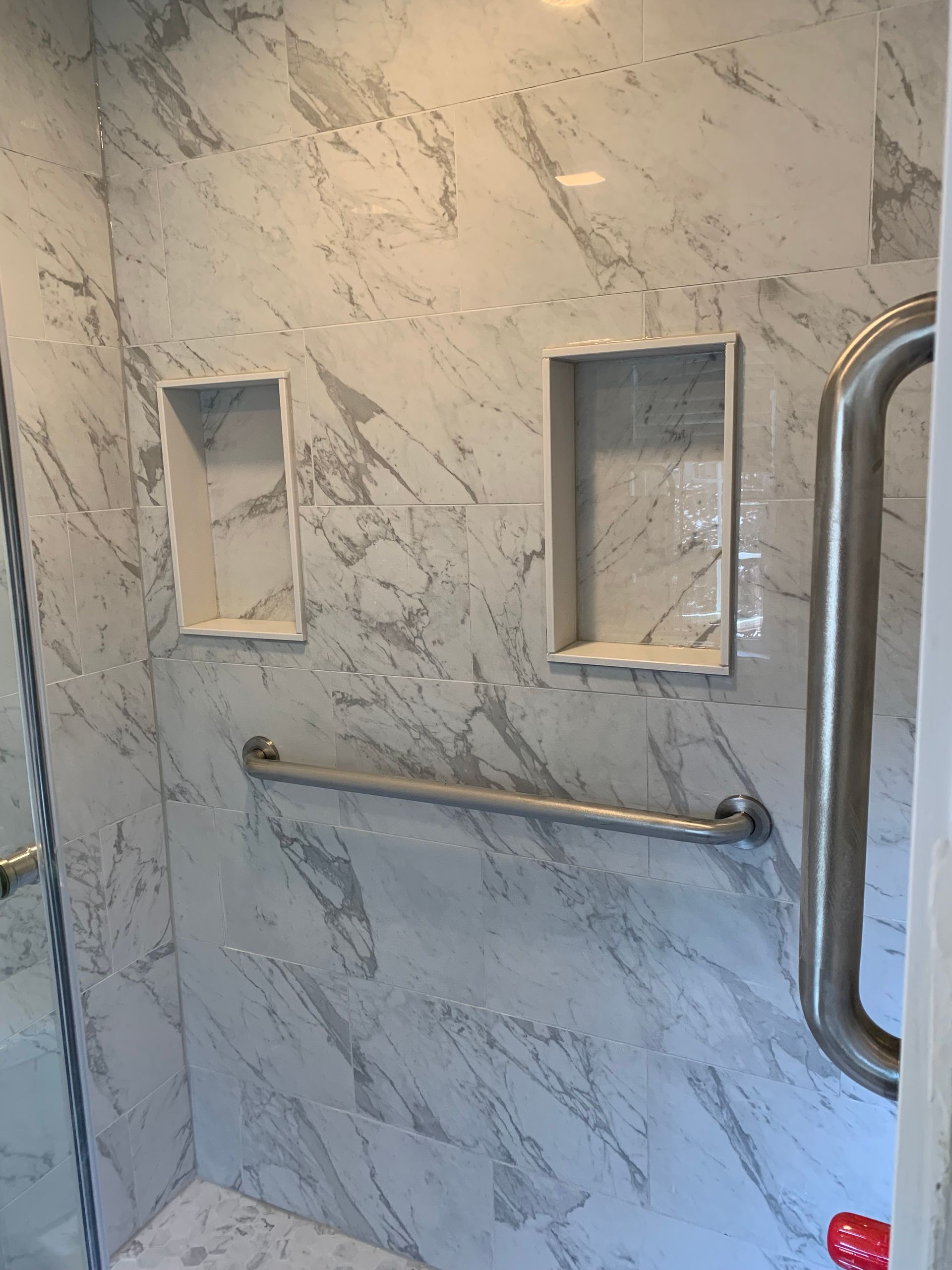 Marble-tiled shower wall with two recessed shelves and a stainless grab bar