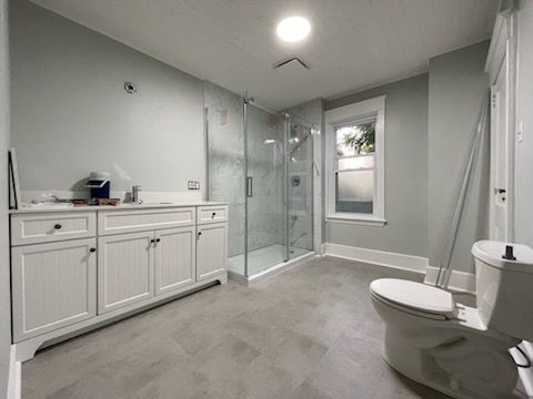 Modern white bathroom with double vanity, glass shower, and toilet on gray tile floor