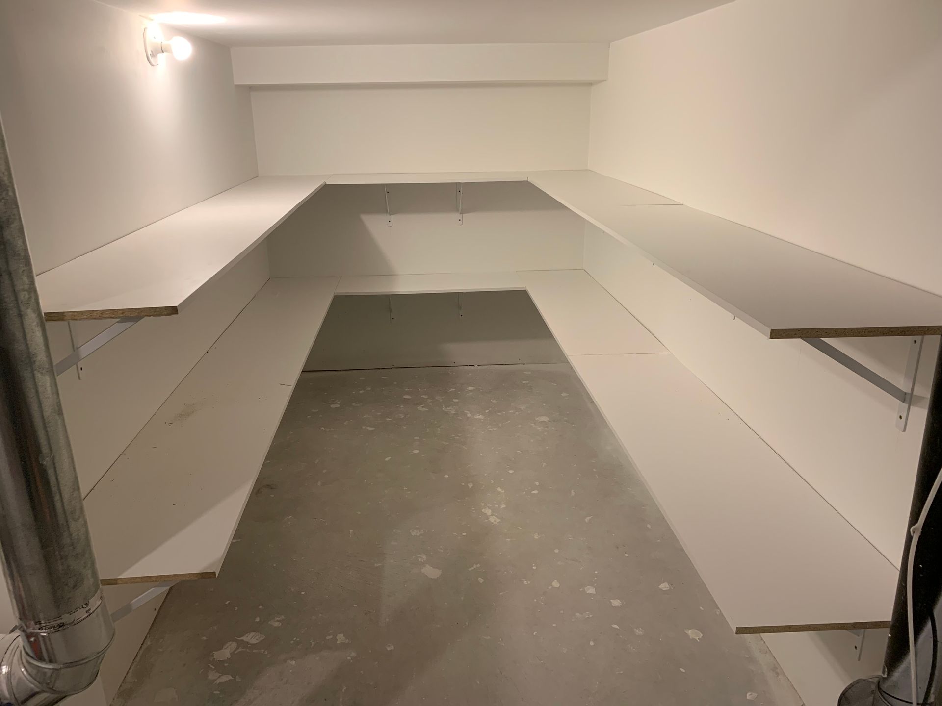 Empty white room with built-in shelves and a concrete floor, like a storage or utility space