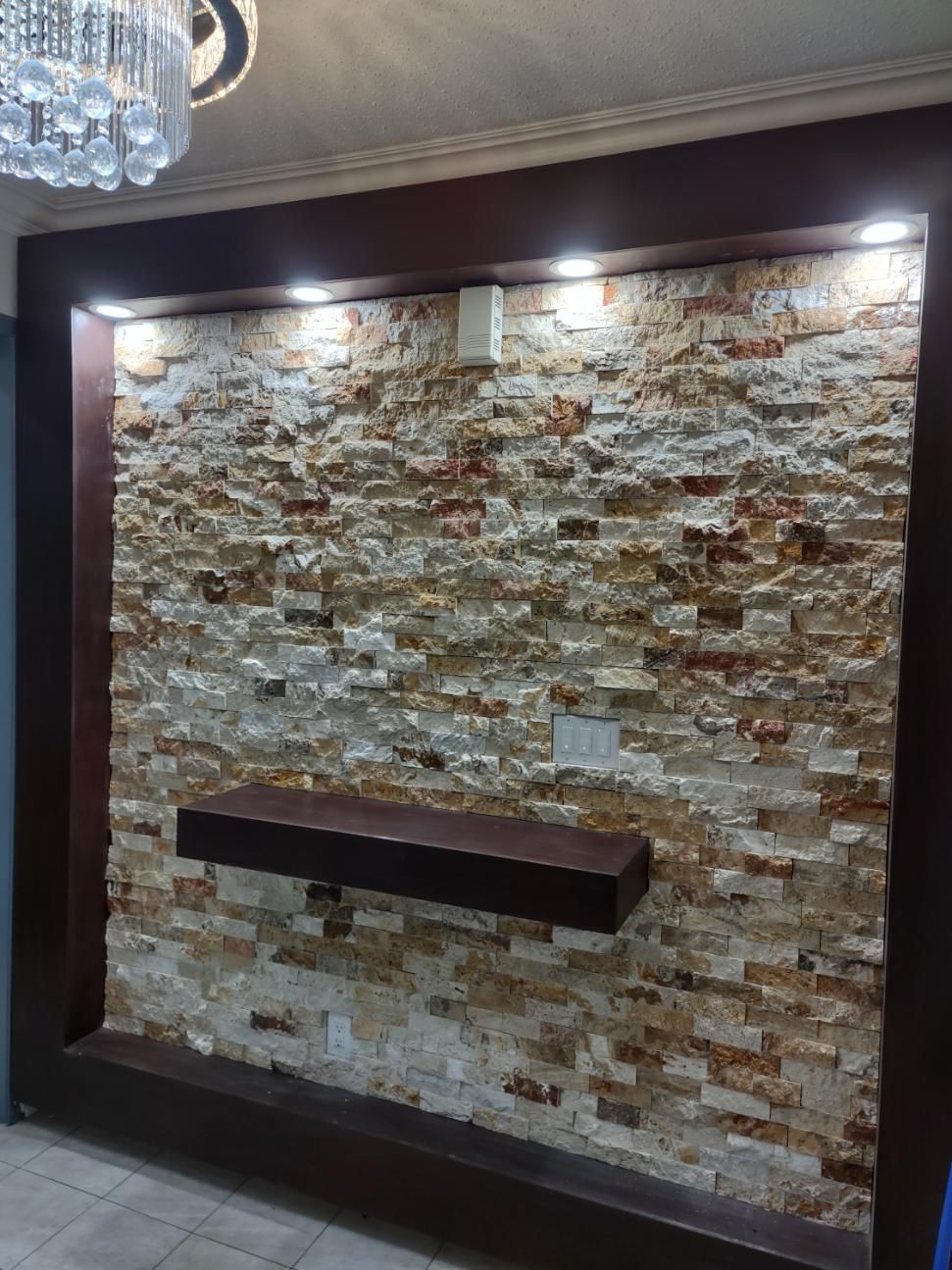 Stone accent wall with a floating dark shelf and recessed lights in a modern room