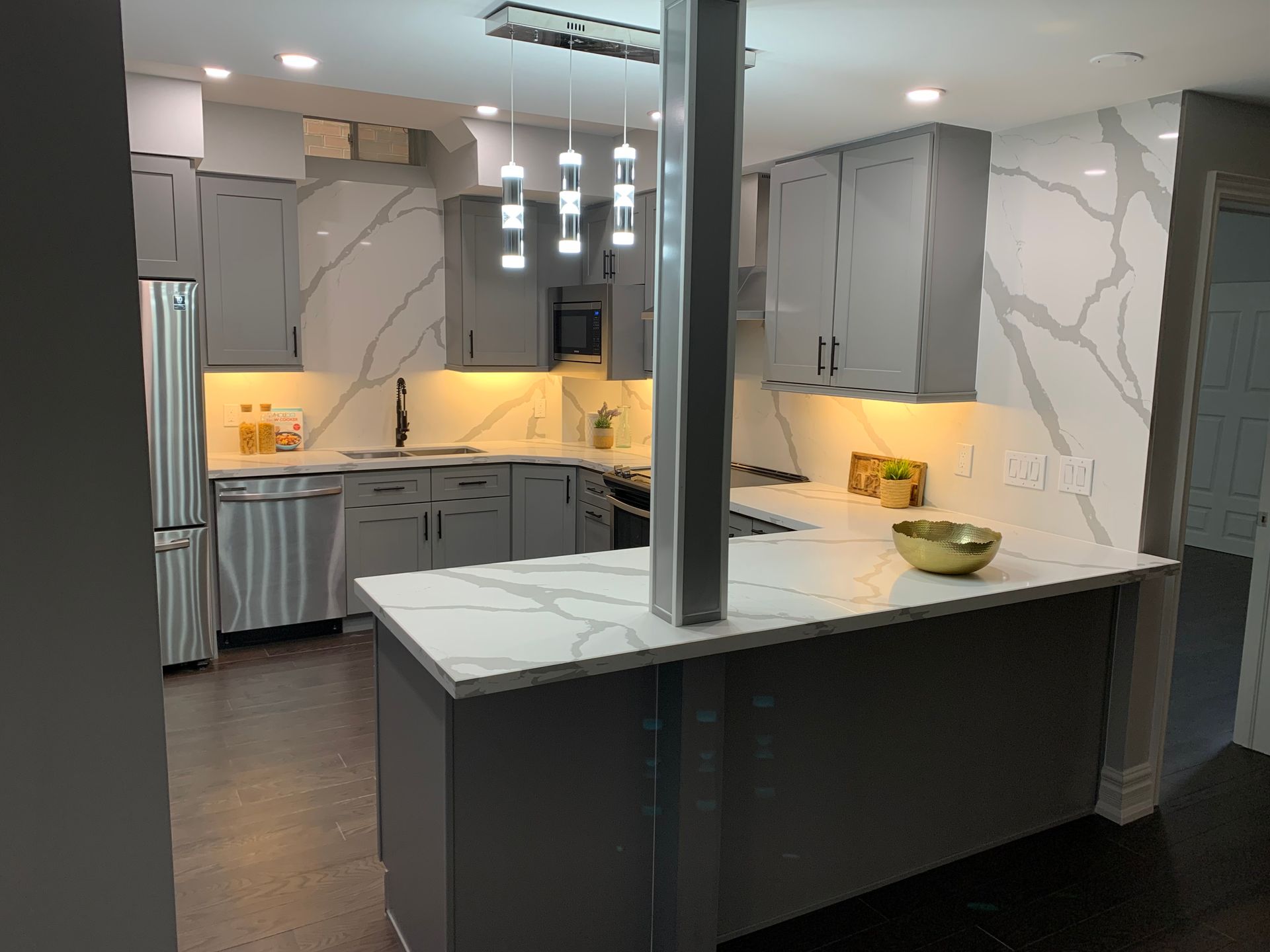 Modern kitchen with gray cabinets, white marble-style counters, pendant lights, and a dark island